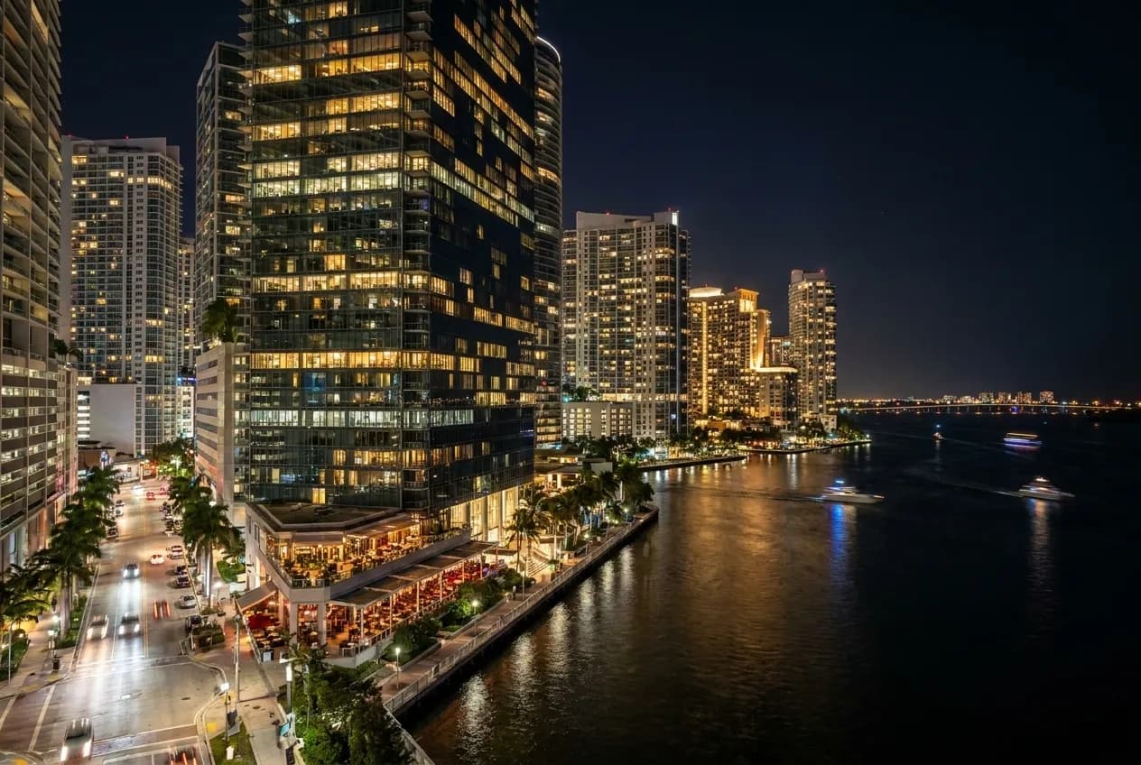Night view of illuminated Brickell glass towers rising above Biscayne Bay with city lights reflecting off office façades and waterfront promenades below