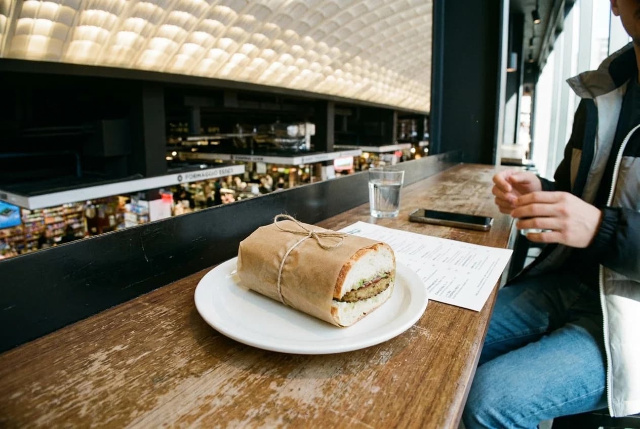 Meatless sandwich in wax paper on white plate at restaurant counter