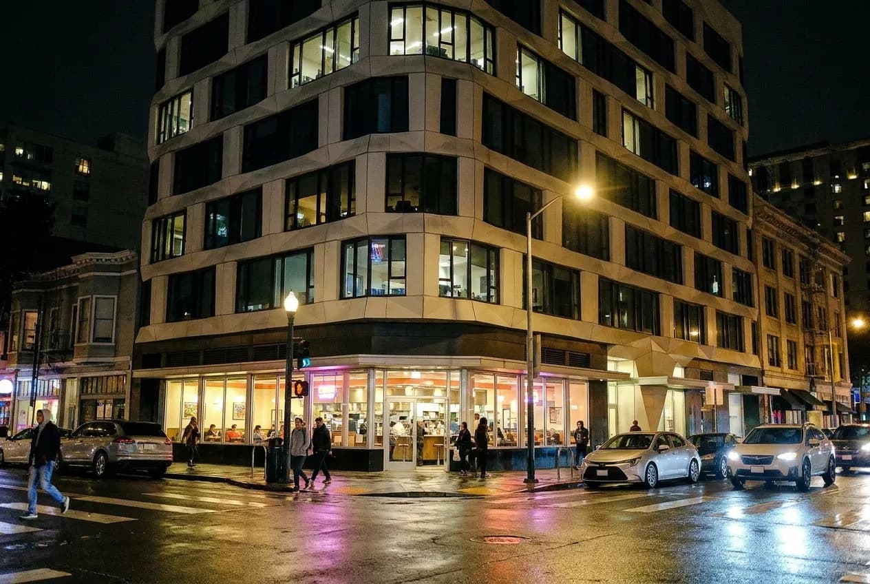 A city street at night with a lit diner window and wet pavement