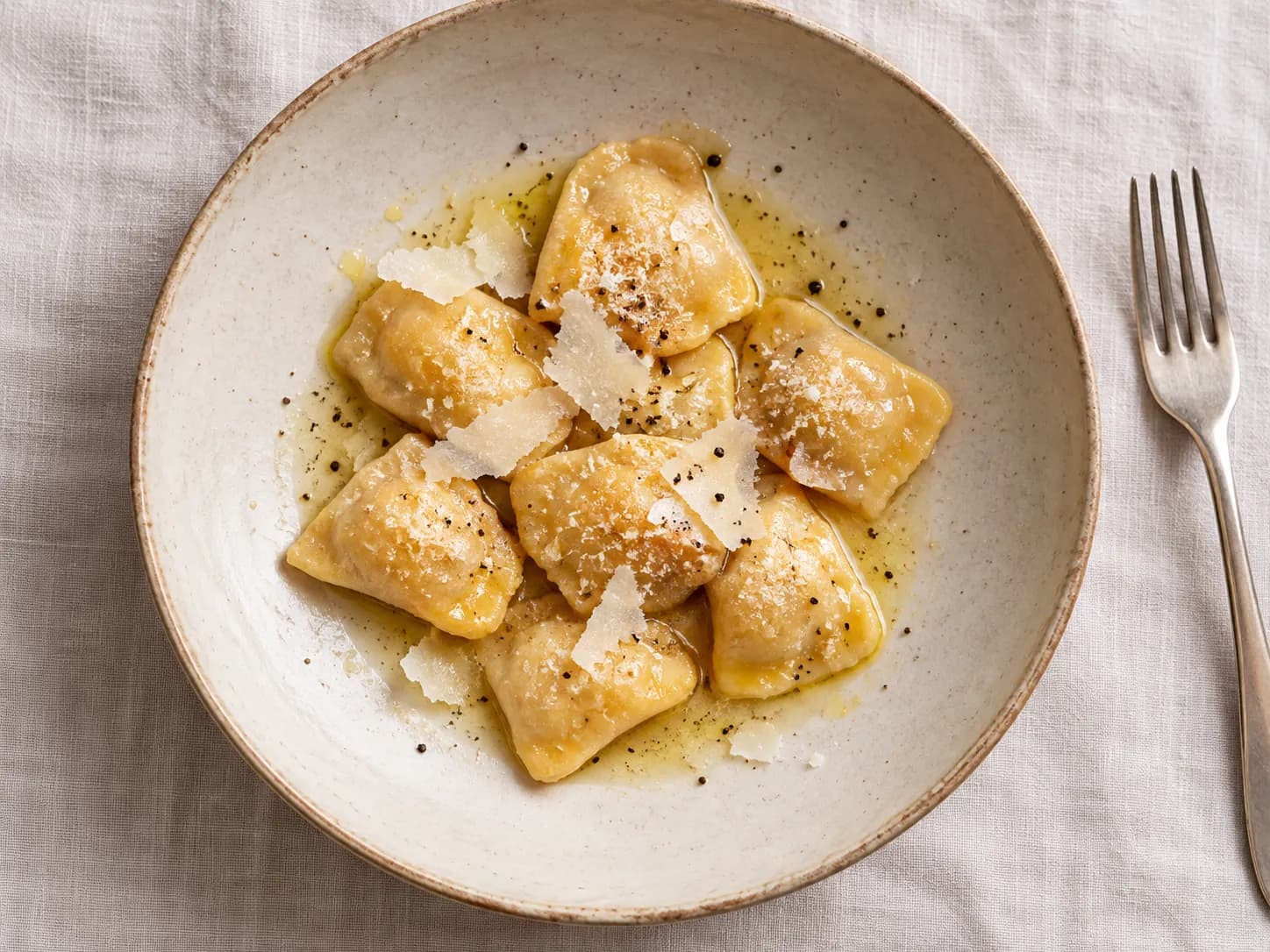 Small folded pasta parcels arranged in a shallow bowl with a thin butter sauce and shaved cheese, photographed from directly above