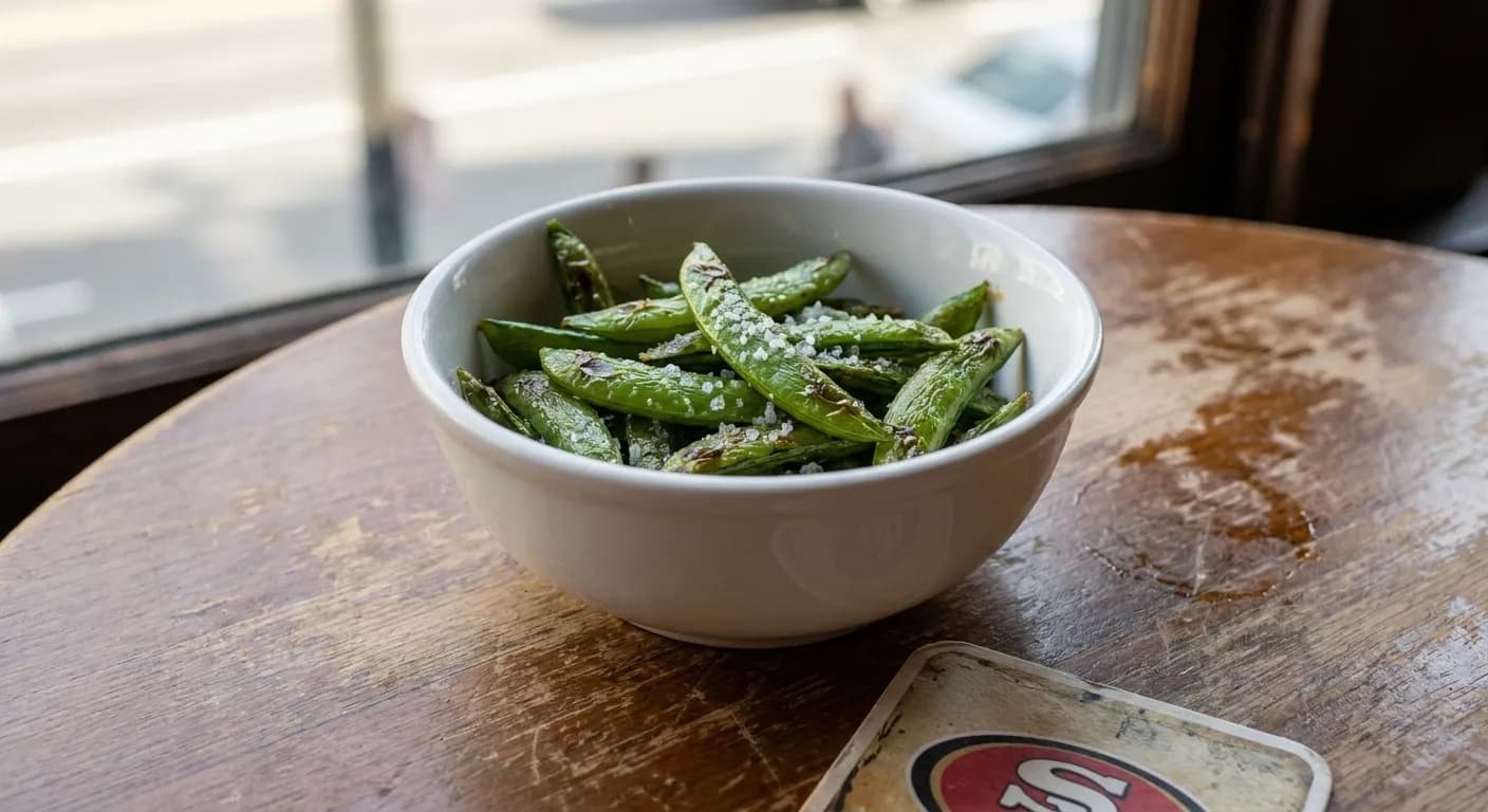 Bowl of roasted sugar snap peas appetizer with sea salt on white ceramic dish at sports bar table