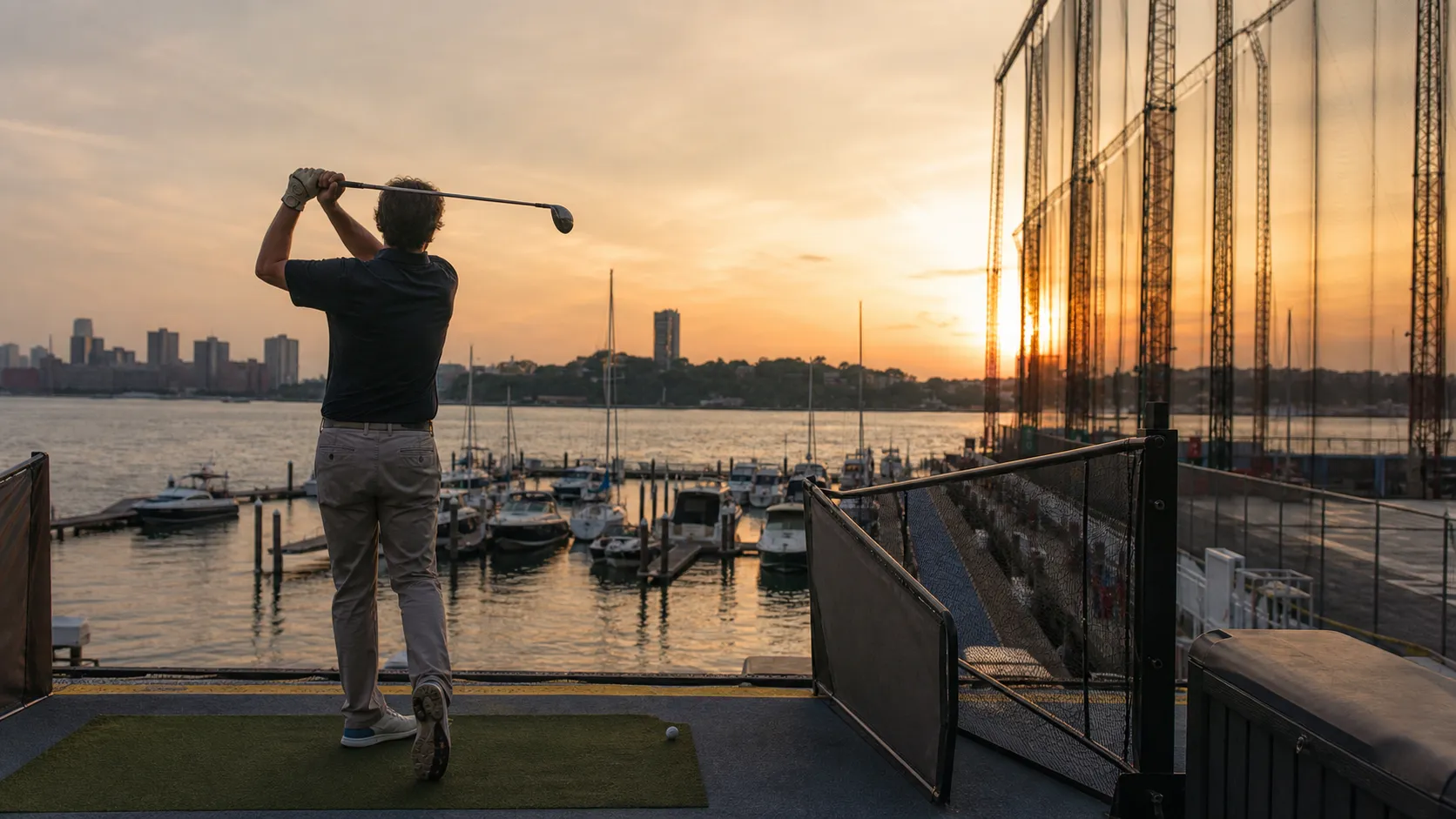 A golfer practices at a Hudson River driving range in Manhattan at golden hour.