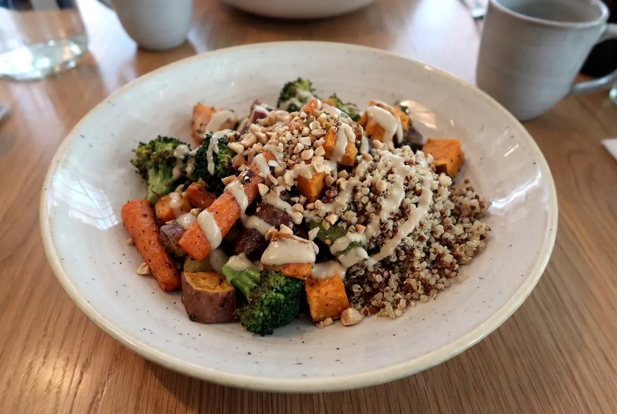 A grain bowl with quinoa, roasted vegetables and a drizzle of tahini in a wide bowl