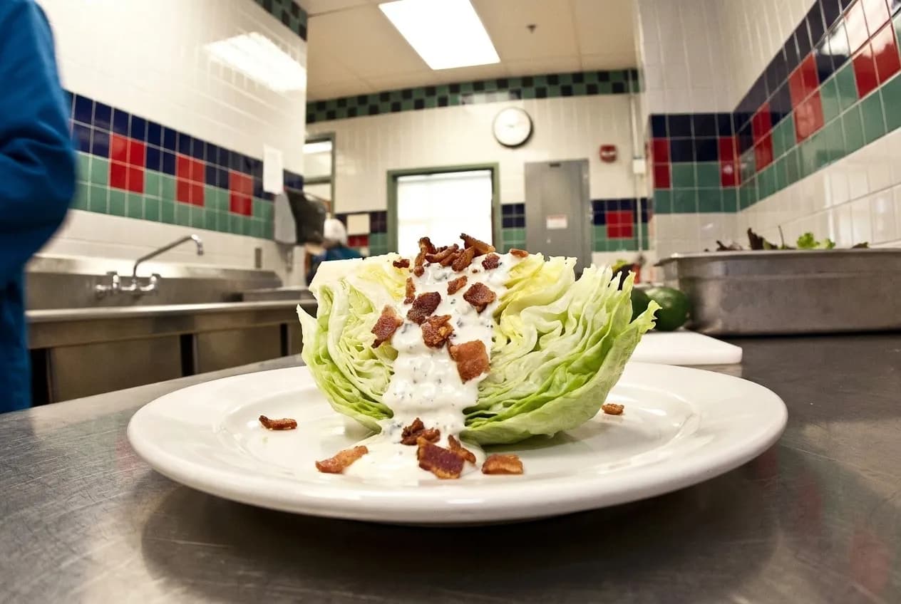 A wedge of crisp lettuce topped with dressing and bacon pieces on a white plate