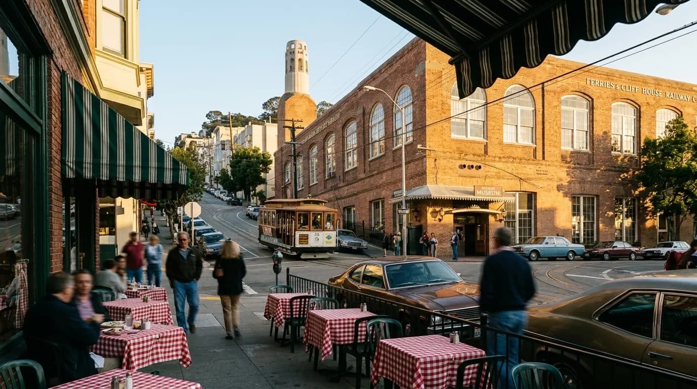 Columbus Avenue in North Beach with sidewalk cafes and Coit Tower visible in the distance under late afternoon sun