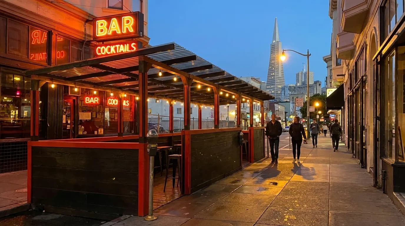 Columbus Avenue in North Beach at night with neon bar signs and pedestrians walking uphill under streetlights