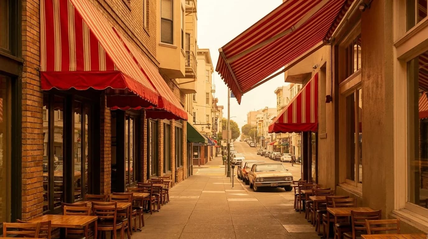Columbus Avenue in San Francisco's North Beach neighborhood on a sunny afternoon, with cafe awnings and sloping sidewalk