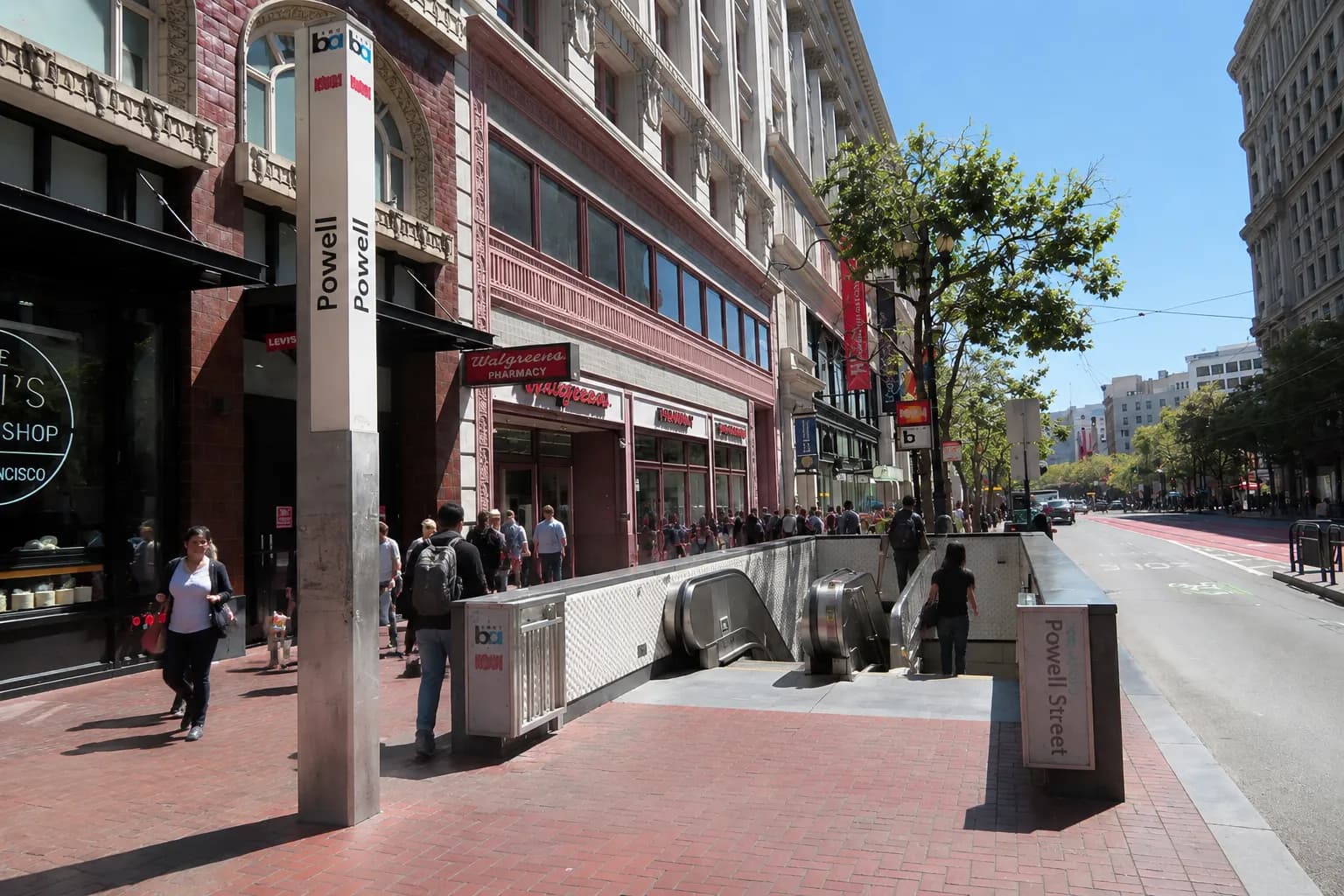 Powell Street BART station entrance with commuters descending stairs in afternoon light