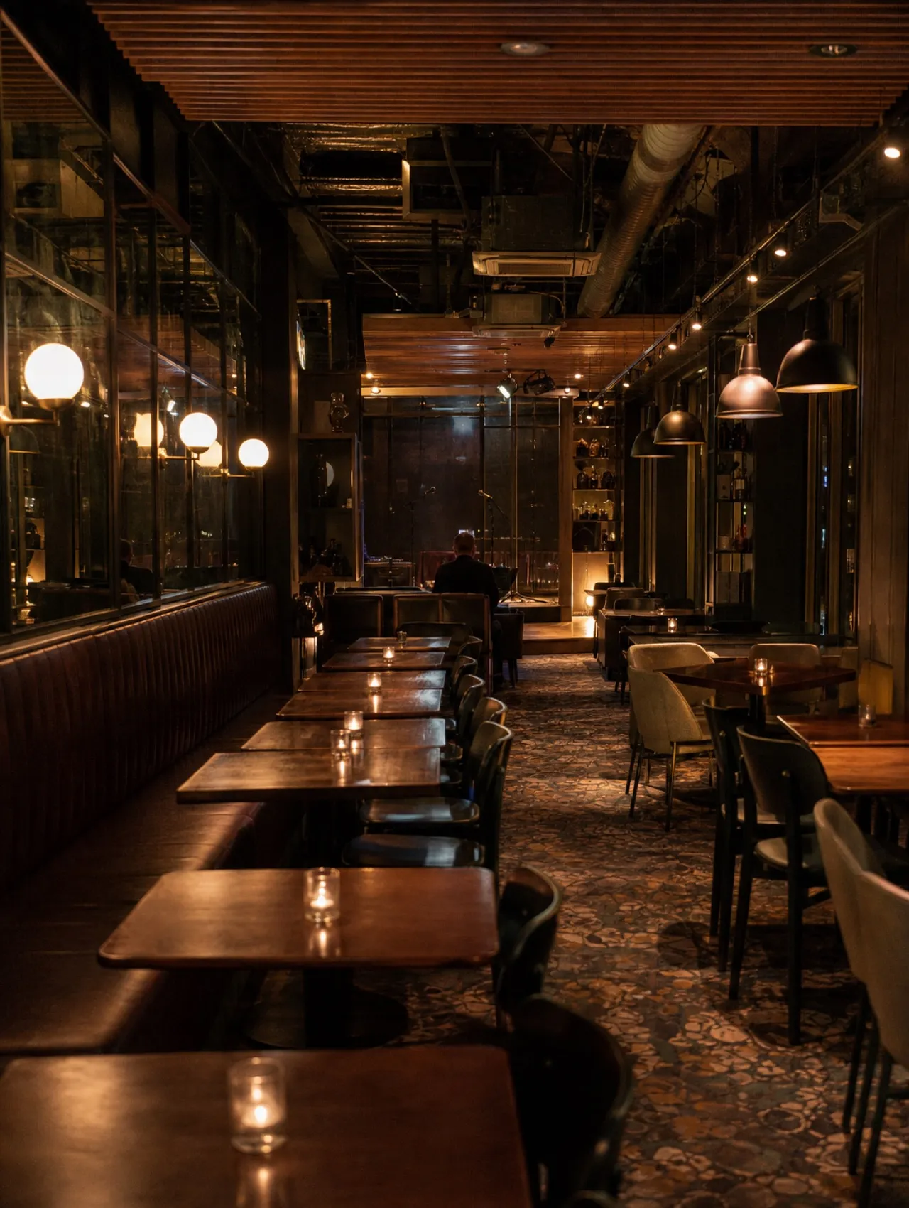 Small dark lounge interior with banquette seating and a low stage area