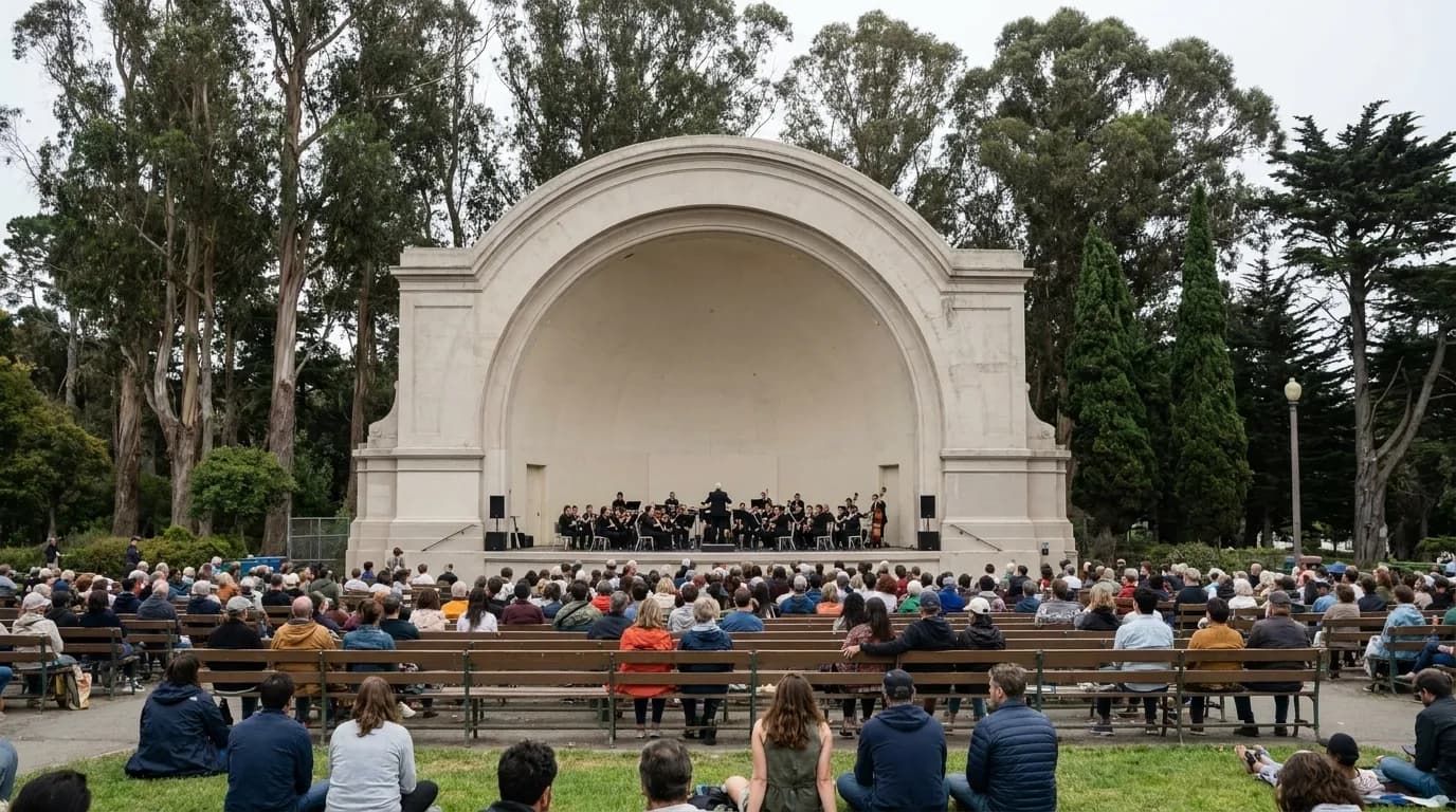 A free outdoor concert at a park bandshell in San Francisco, an audience on the grass in front of a curved concrete shell with eucalyptus trees and pale afternoon light
