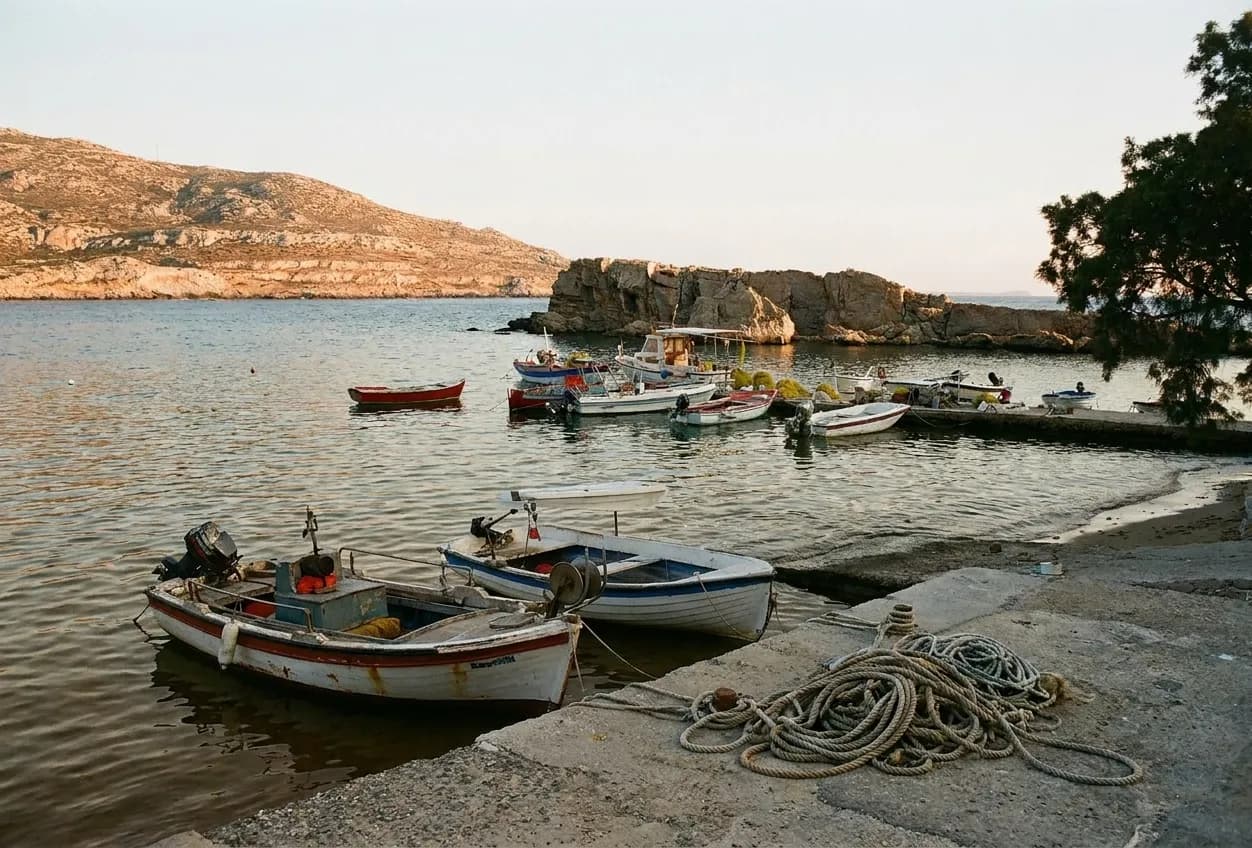 Small boats moored along a concrete seawall with coiled rope in the foreground and low evening light on the water