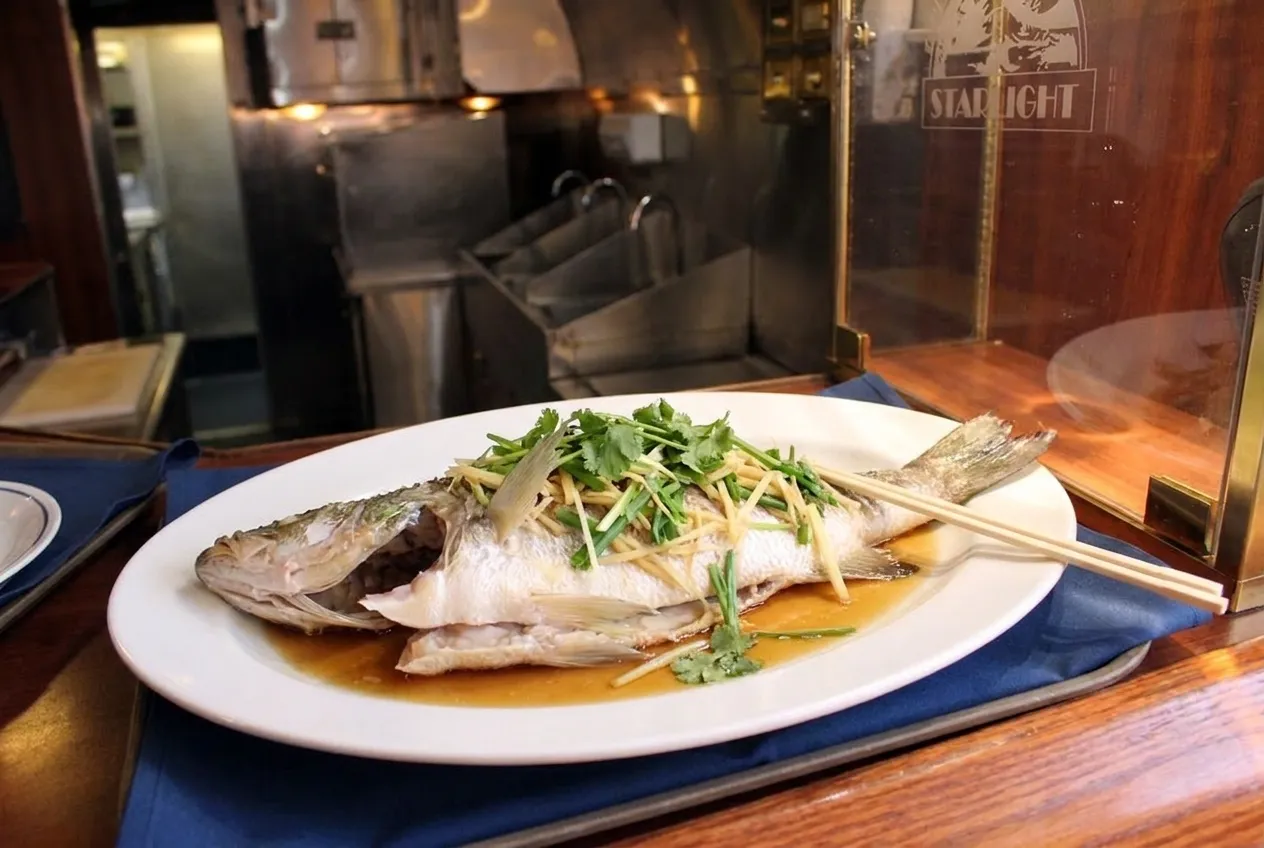 Whole steamed fish with ginger and scallions on a white platter