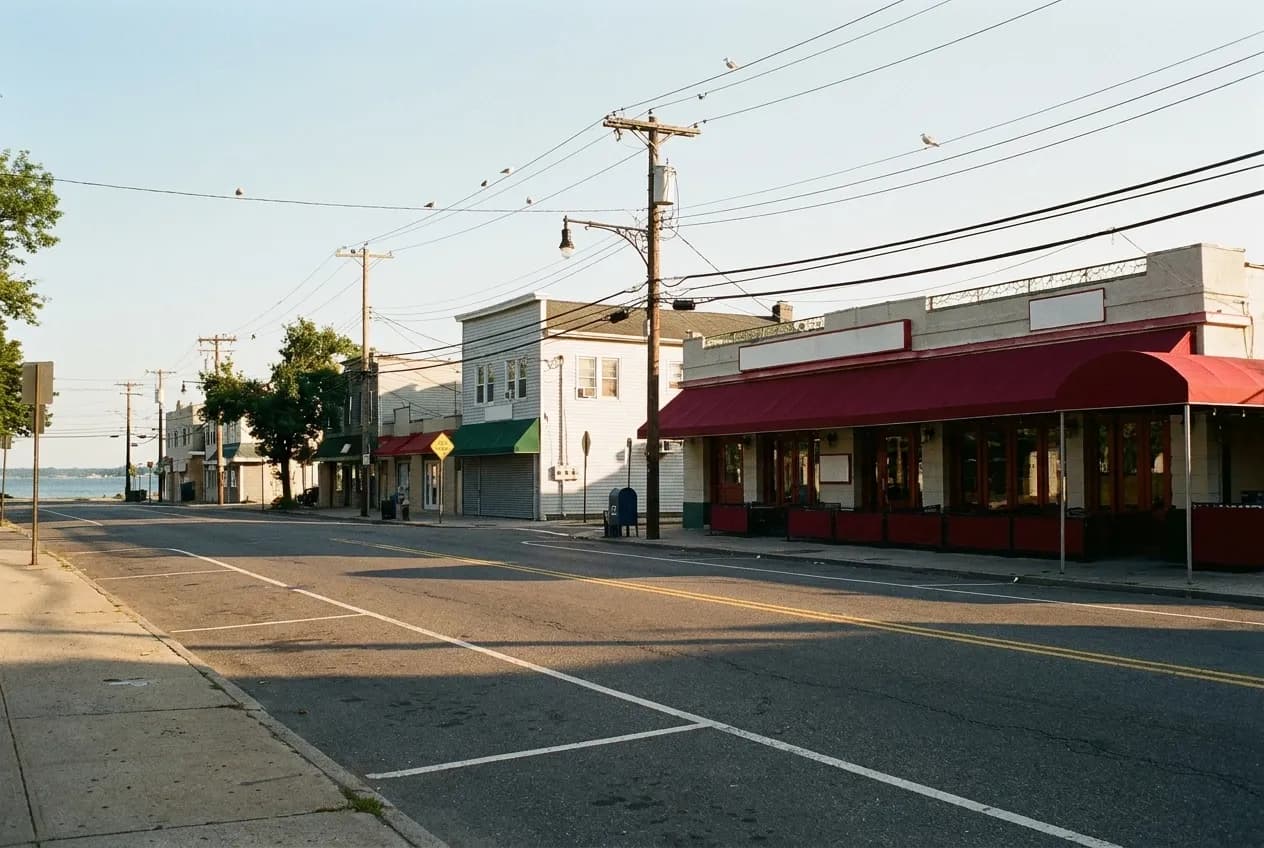 Low-rise seafood restaurant row along City Island Avenue in the Bronx in late afternoon light, awnings and utility wires with the Sound at the far end