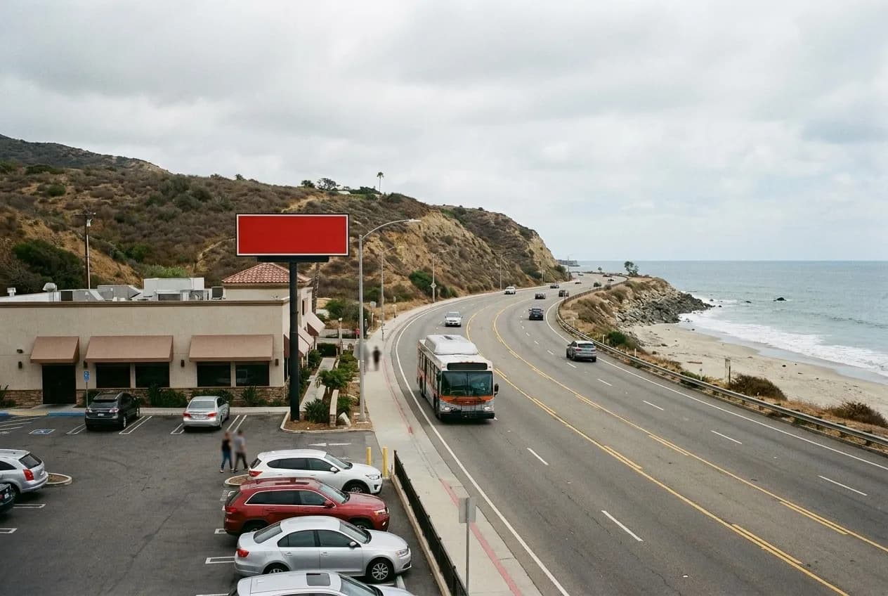 A coastal highway curving beside the ocean with dry hills above