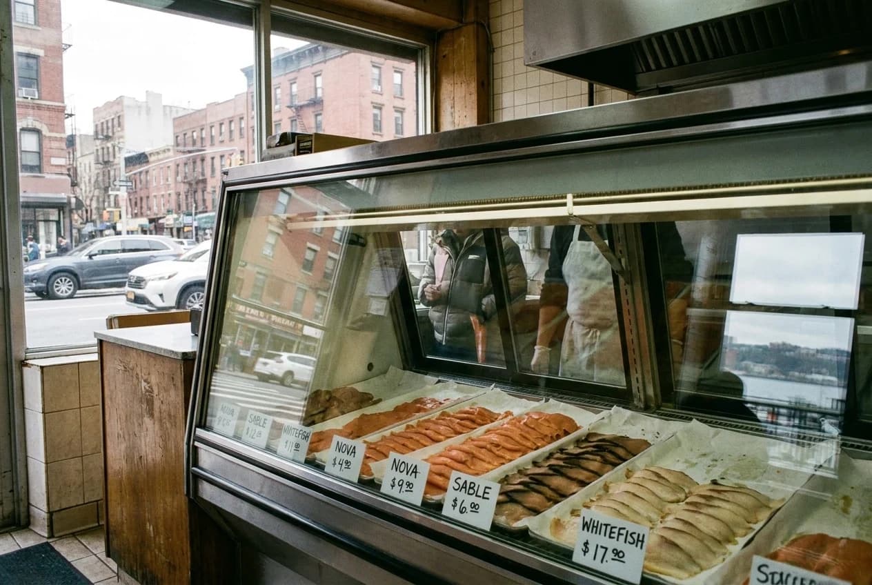 Refrigerated display case with sliced smoked salmon, sable, and whitefish on white paper with price cards