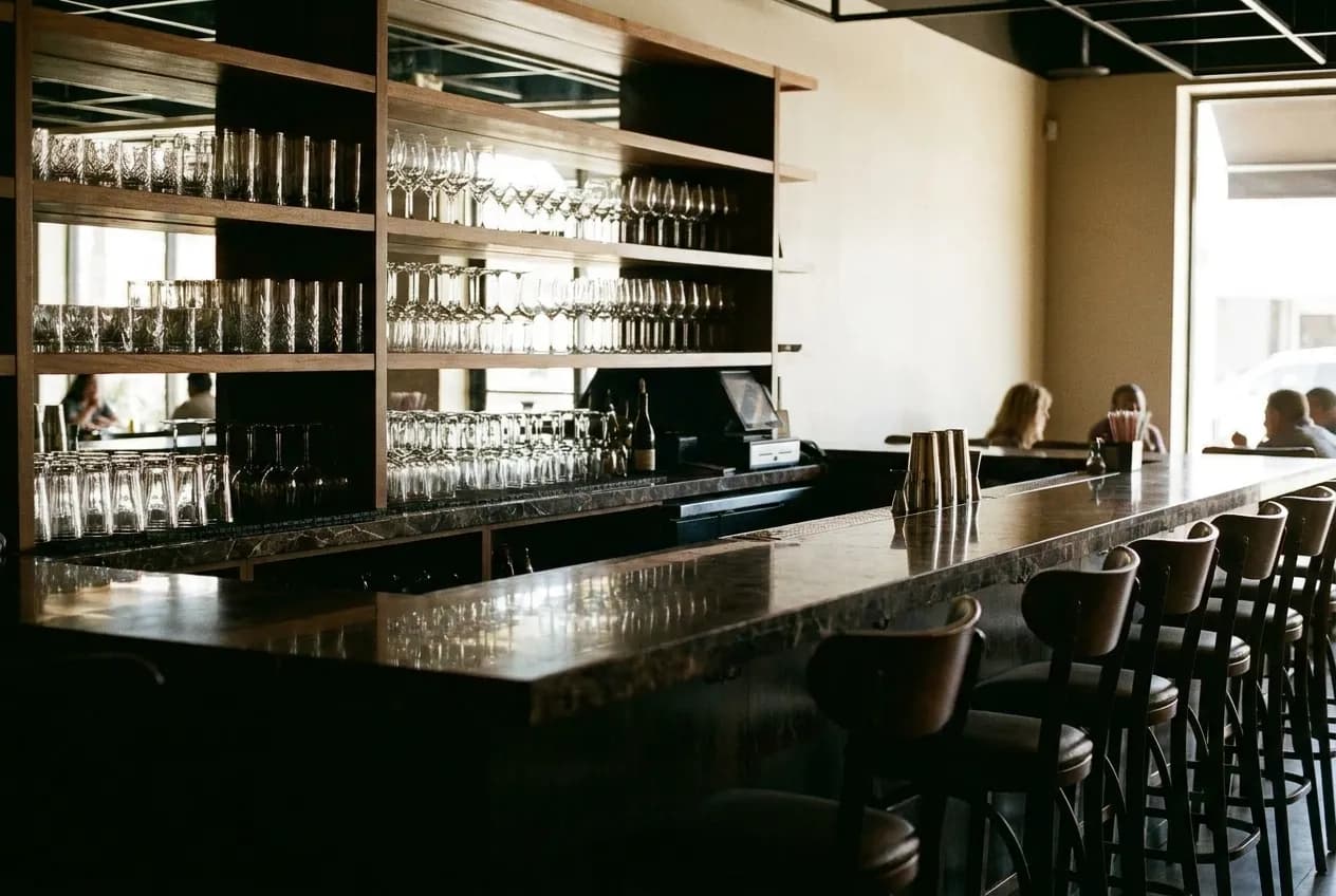 A marble bar counter with stools and shelves of glassware behind it in a small restaurant