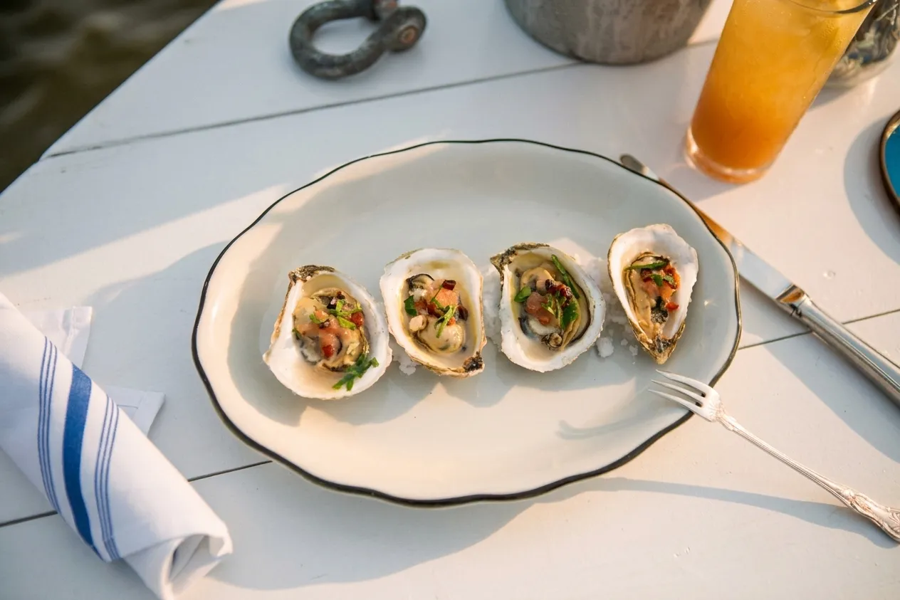 Freshly shucked oysters on a white deck table at golden hour with the Hudson River behind