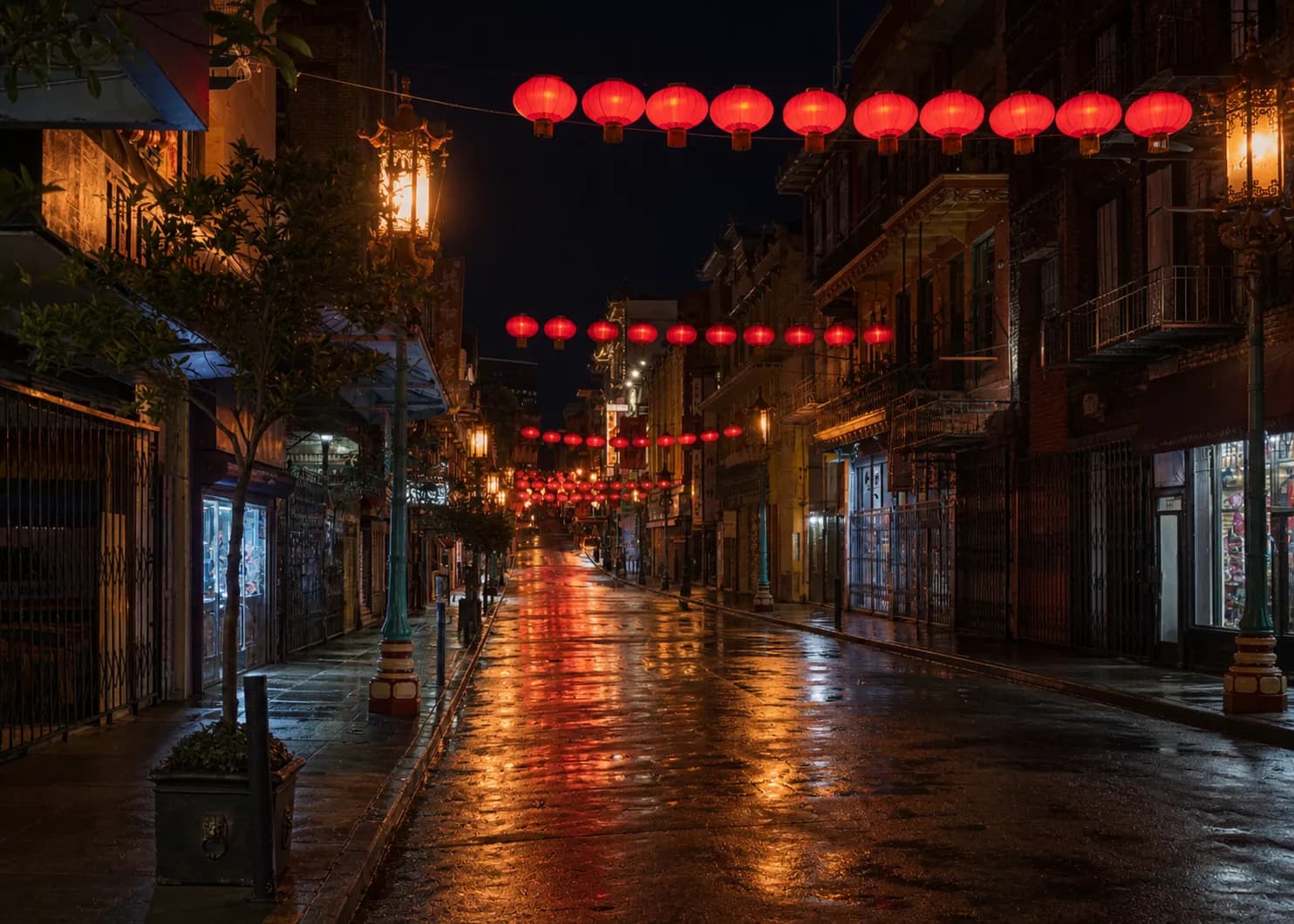 A narrow San Francisco Chinatown street at night with red paper lanterns strung overhead, glowing shopfront windows, iron fire escapes and wet pavement reflecting red and amber light