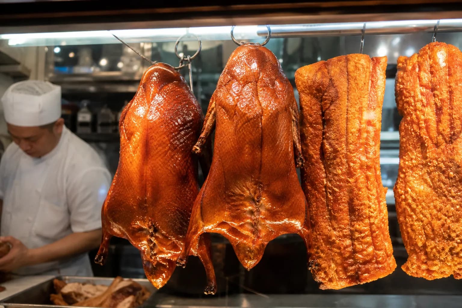 Hanging Cantonese roasted ducks and crispy pork belly at the hot food counter inside the market.