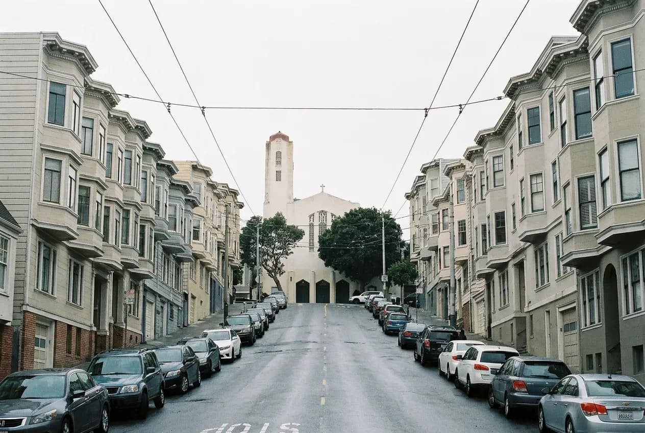 A steep San Francisco street of apartment buildings climbing away from the viewer under a pale sky