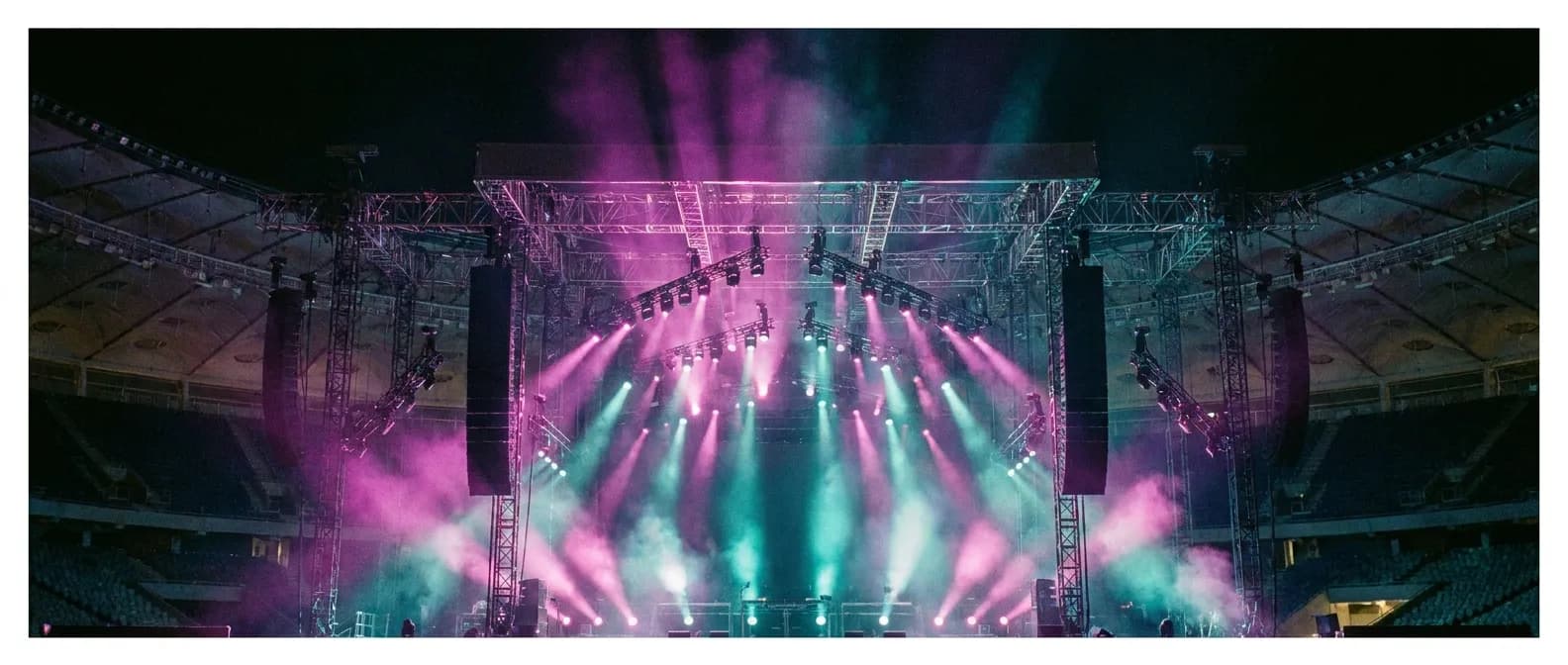A concert stage rig with lights and haze inside a giant stadium bowl at showtime
