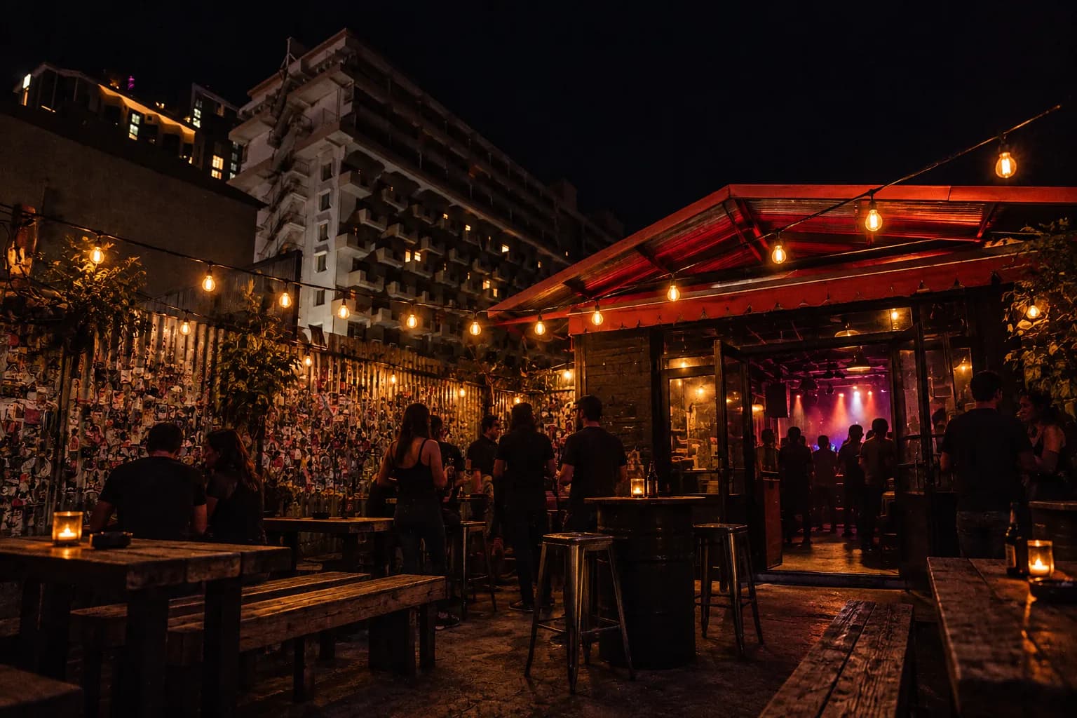 A back patio at night with strung bulbs, benches and people standing in small groups