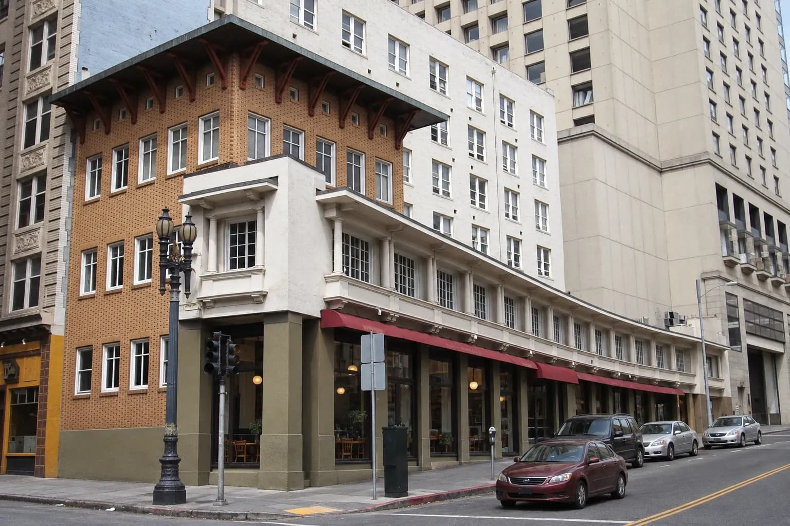A low one-storey restaurant and residential building on a San Francisco street corner, photographed in daylight with a plain facade, pavement, older neighbouring structures and muted grey, cream and brick tones.