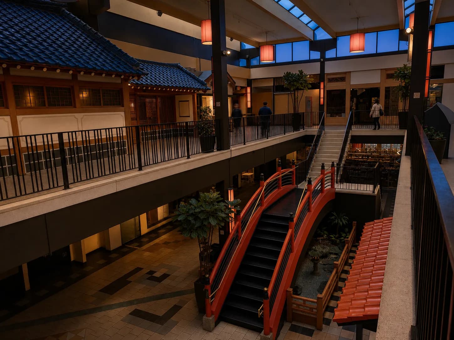 Interior arcade of a Japanese-American shopping center at dusk, with a red arched footbridge, tiled pagoda roofs and paper lanterns