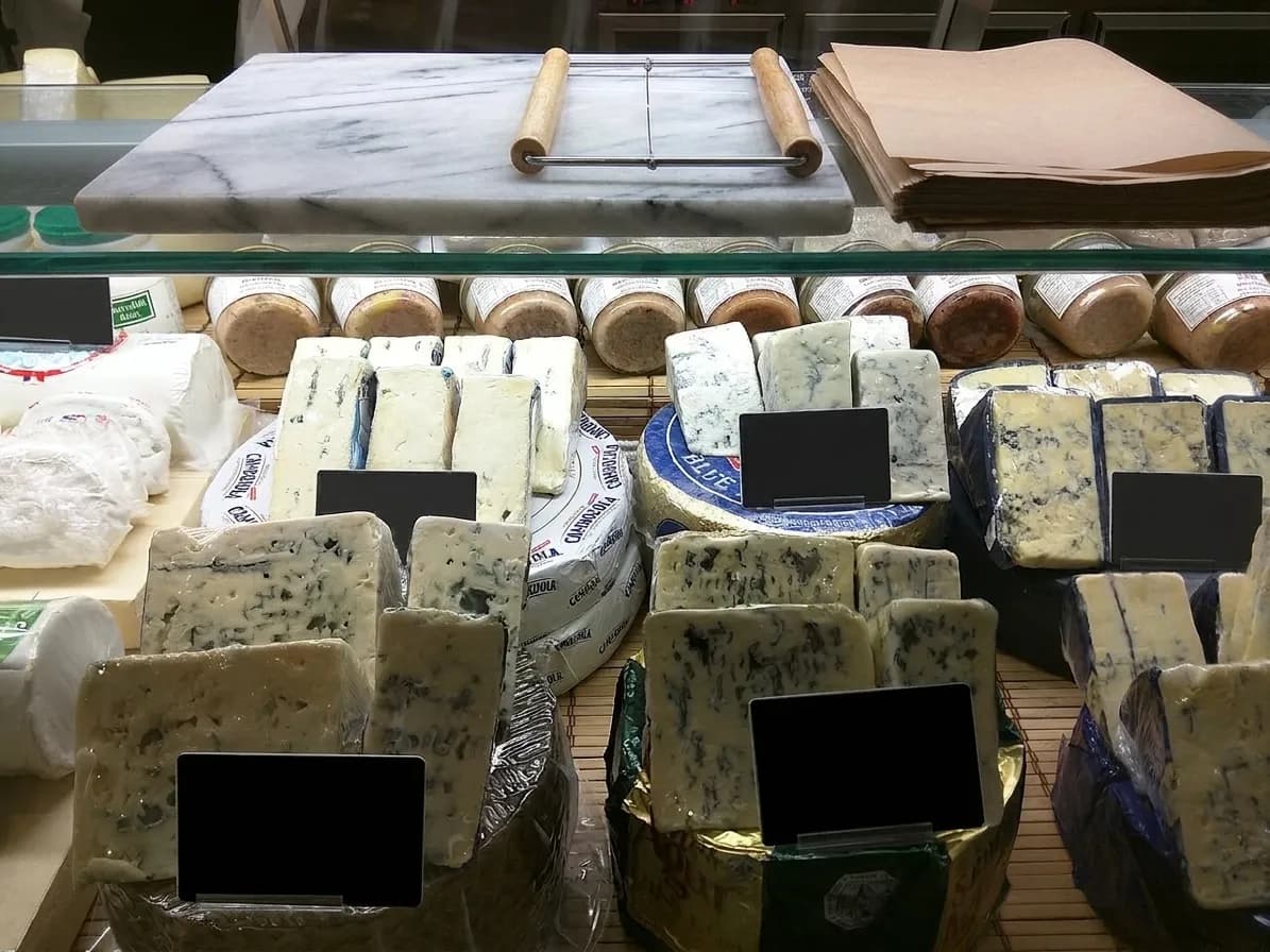 A cheese counter with wheels and wedges arranged behind glass, a wire cutter and a marble slab on top