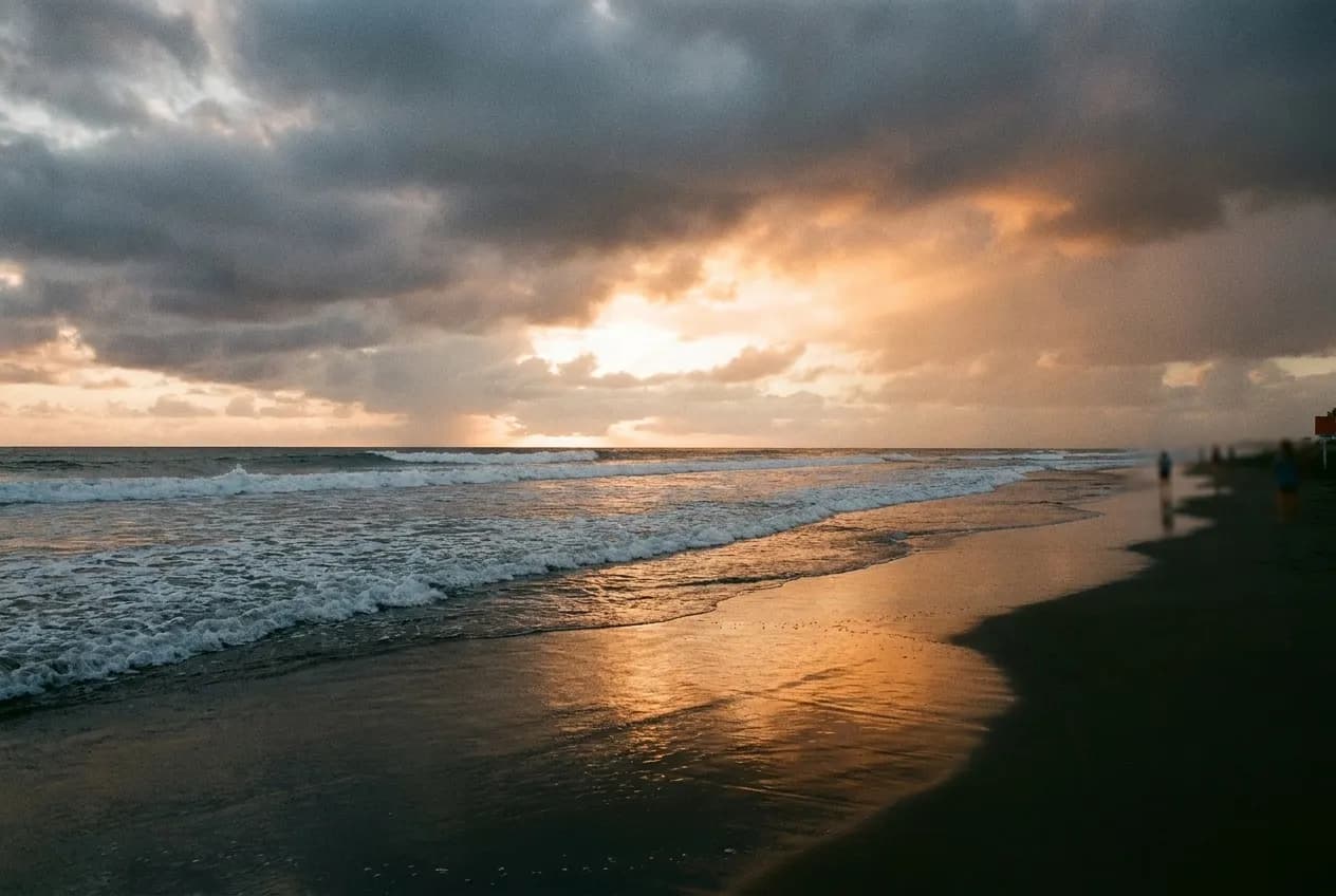 A wide empty beach under low cloud, surf breaking in long lines