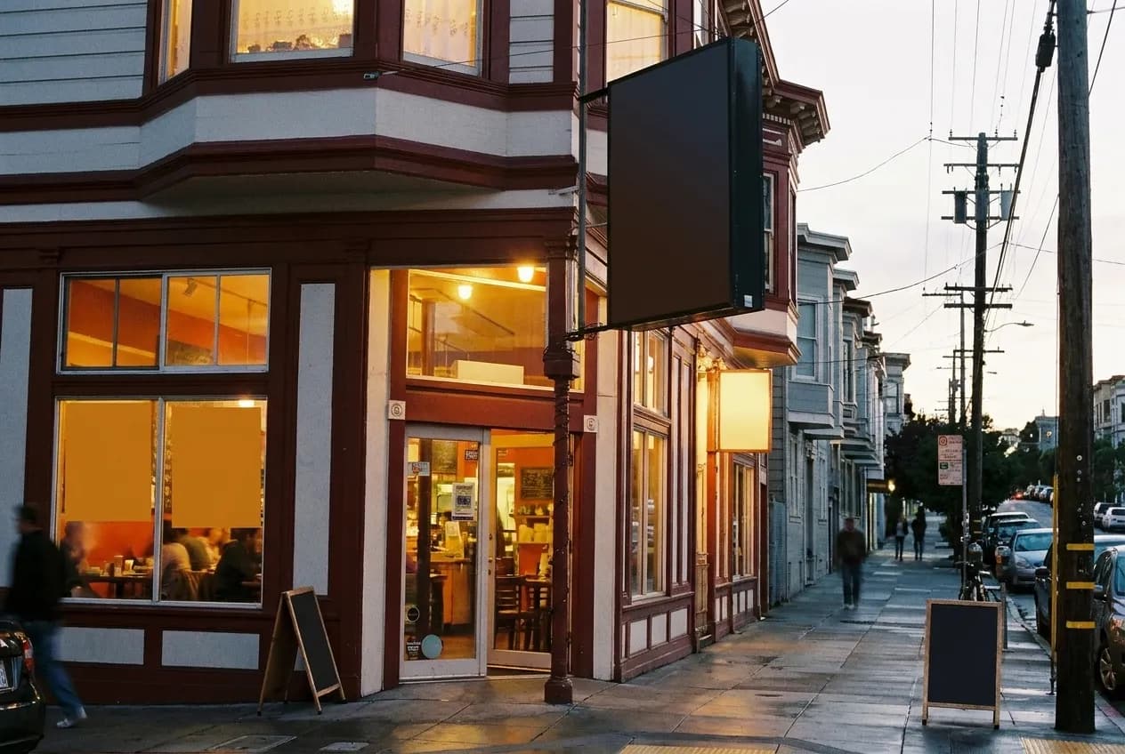 A restaurant frontage at dusk, windows lit, the street sloping away past it
