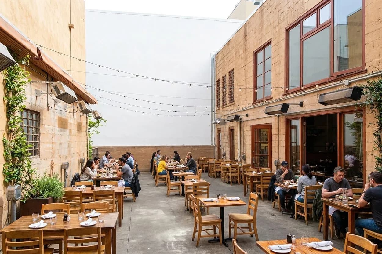 Wide courtyard brunch scene with sunlit tables and leafy surroundings
