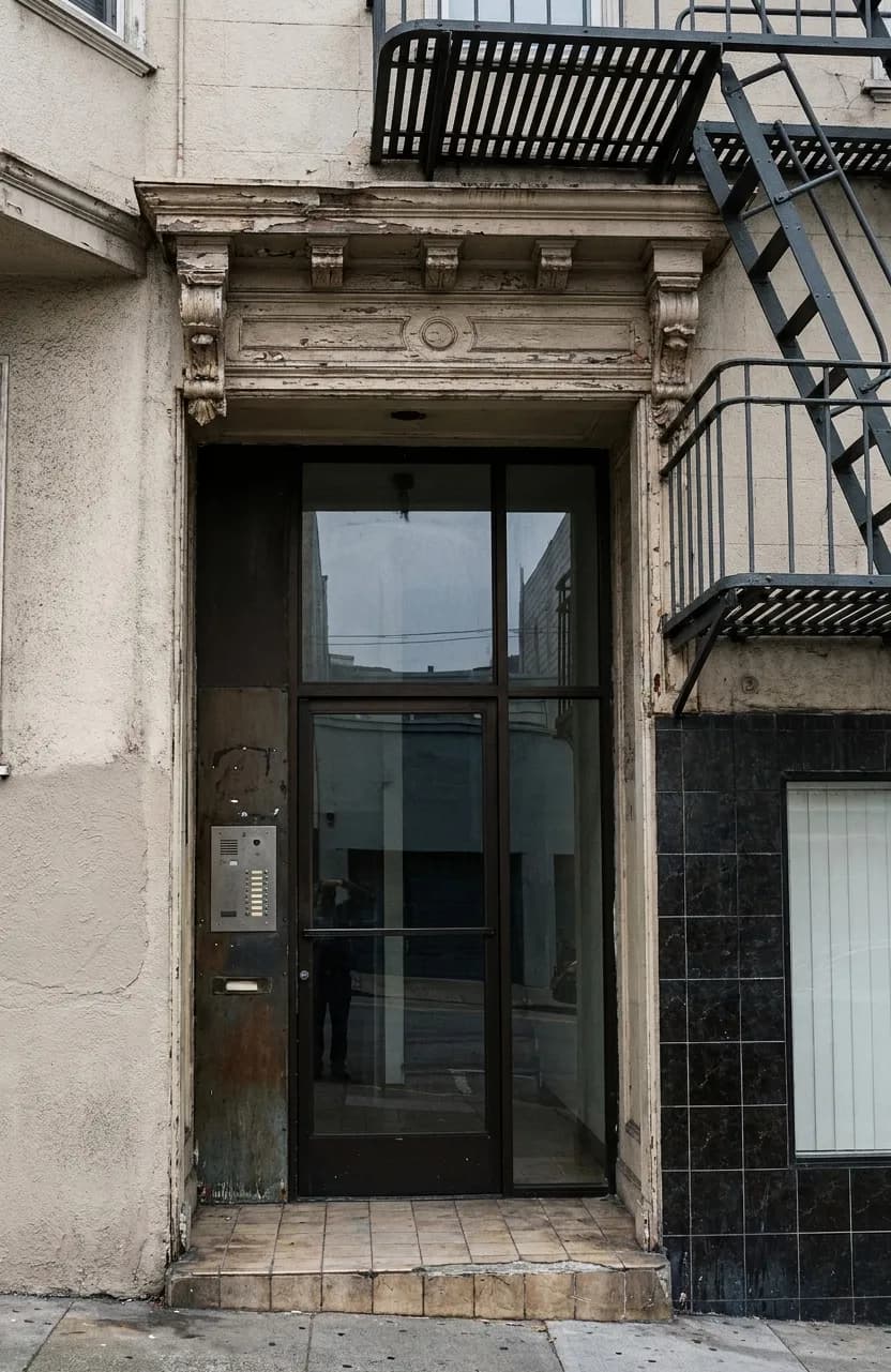 A recessed shop doorway with a dark glass door and intercom on a narrow San Francisco street under fire escapes