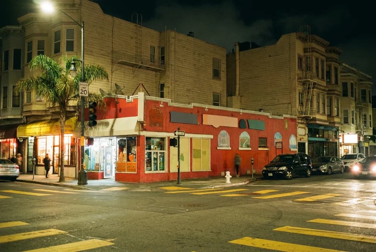 A commercial street after midnight, a few shopfronts still lit along it