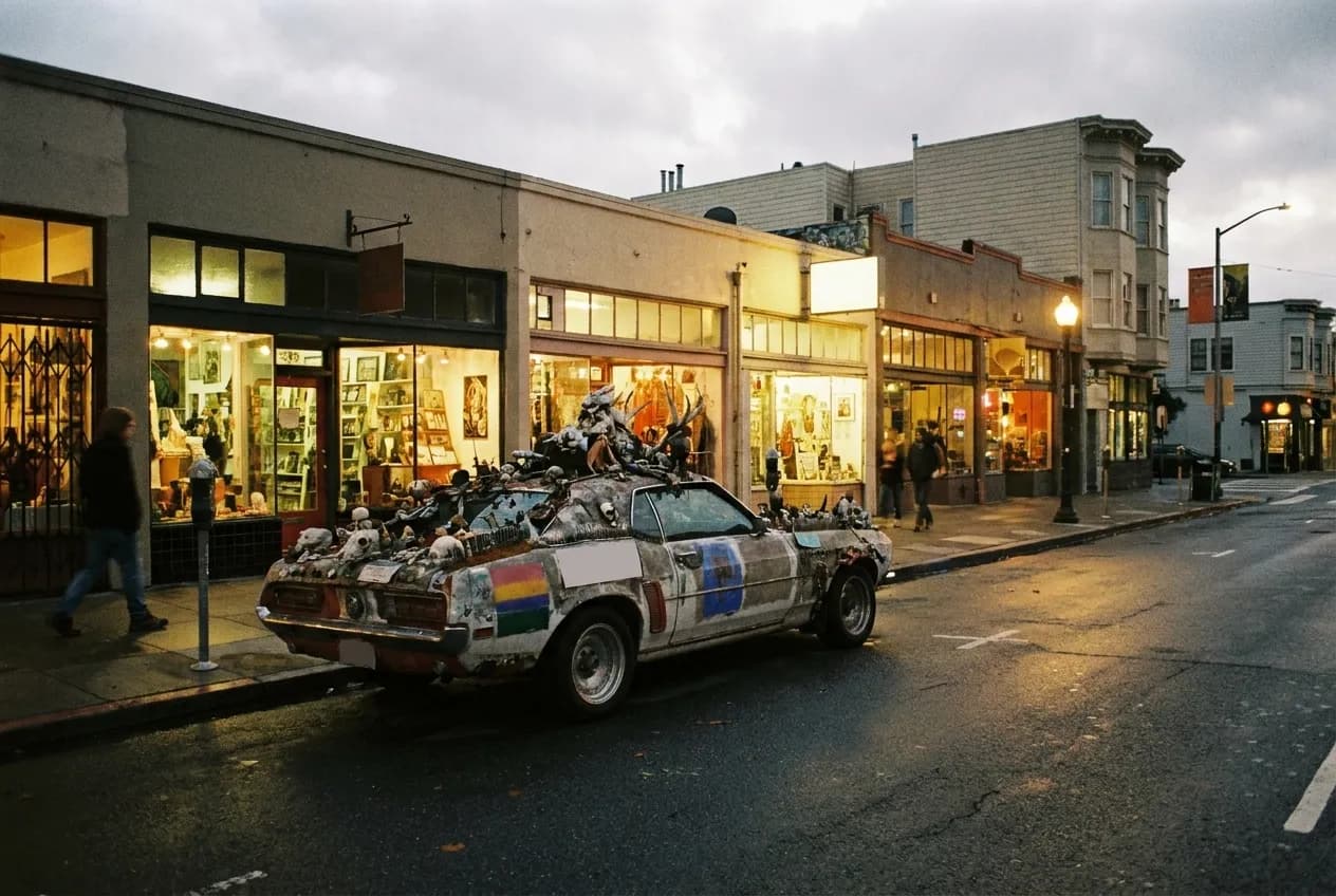 A wide street of low buildings and painted walls after dark, shopfronts still lit