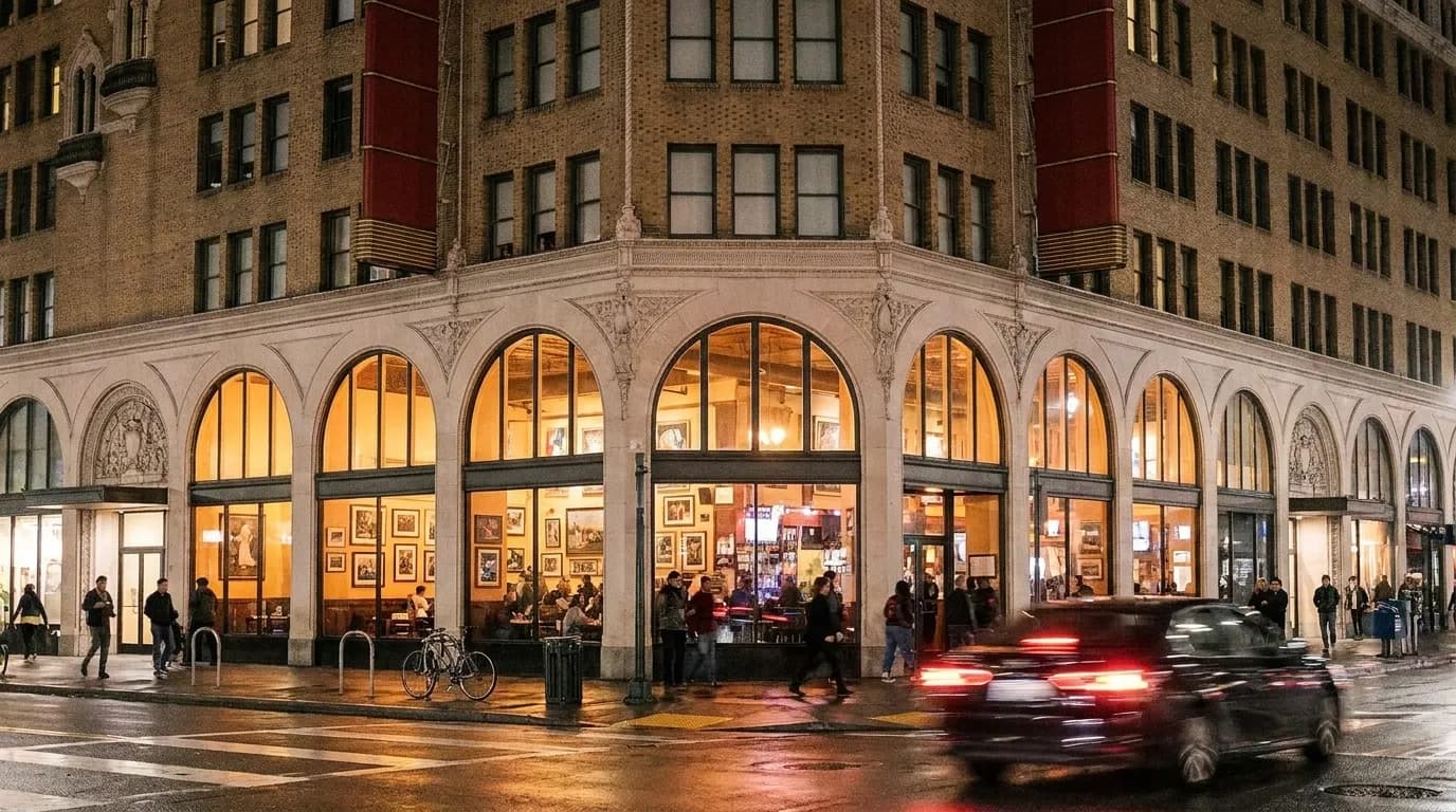A corner bar on Divisadero Street in San Francisco at night with tall windows and art visible on the interior walls.