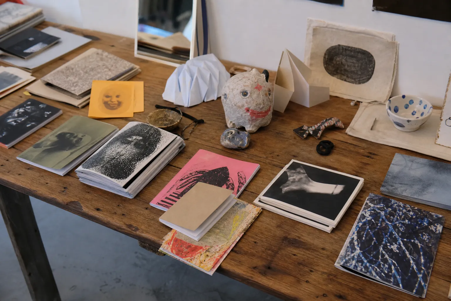 A tabletop of books, zines, and quirky art objects in a Mission-style collection