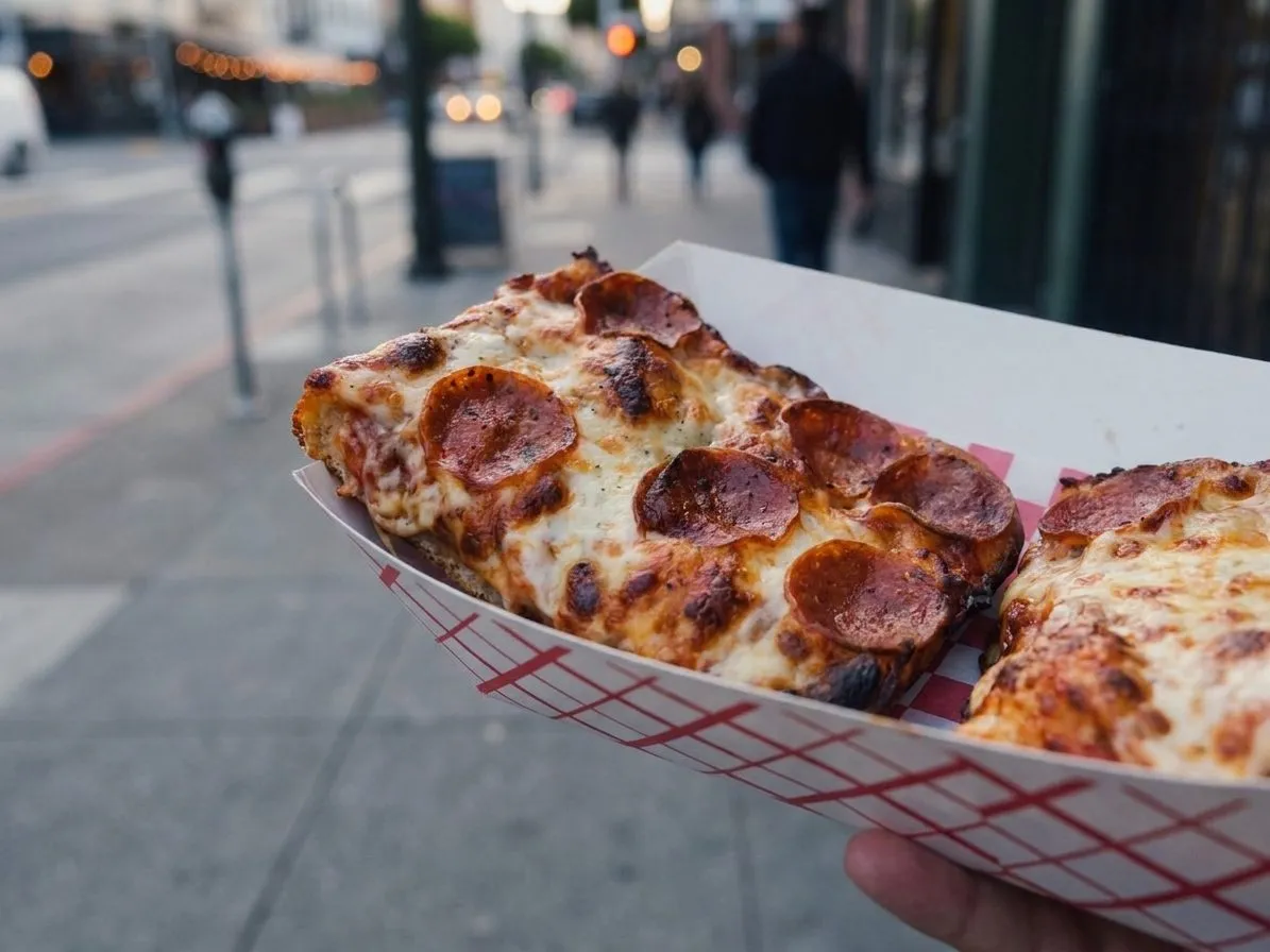 Square pizza slices in a paper tray on a North Beach street