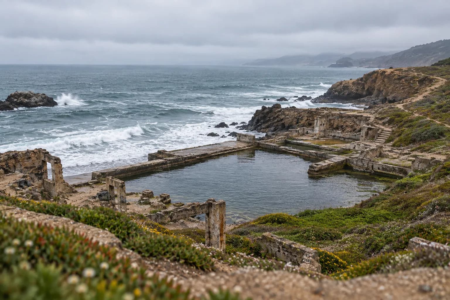 The concrete ruins of a seaside bathhouse against rocks and surf