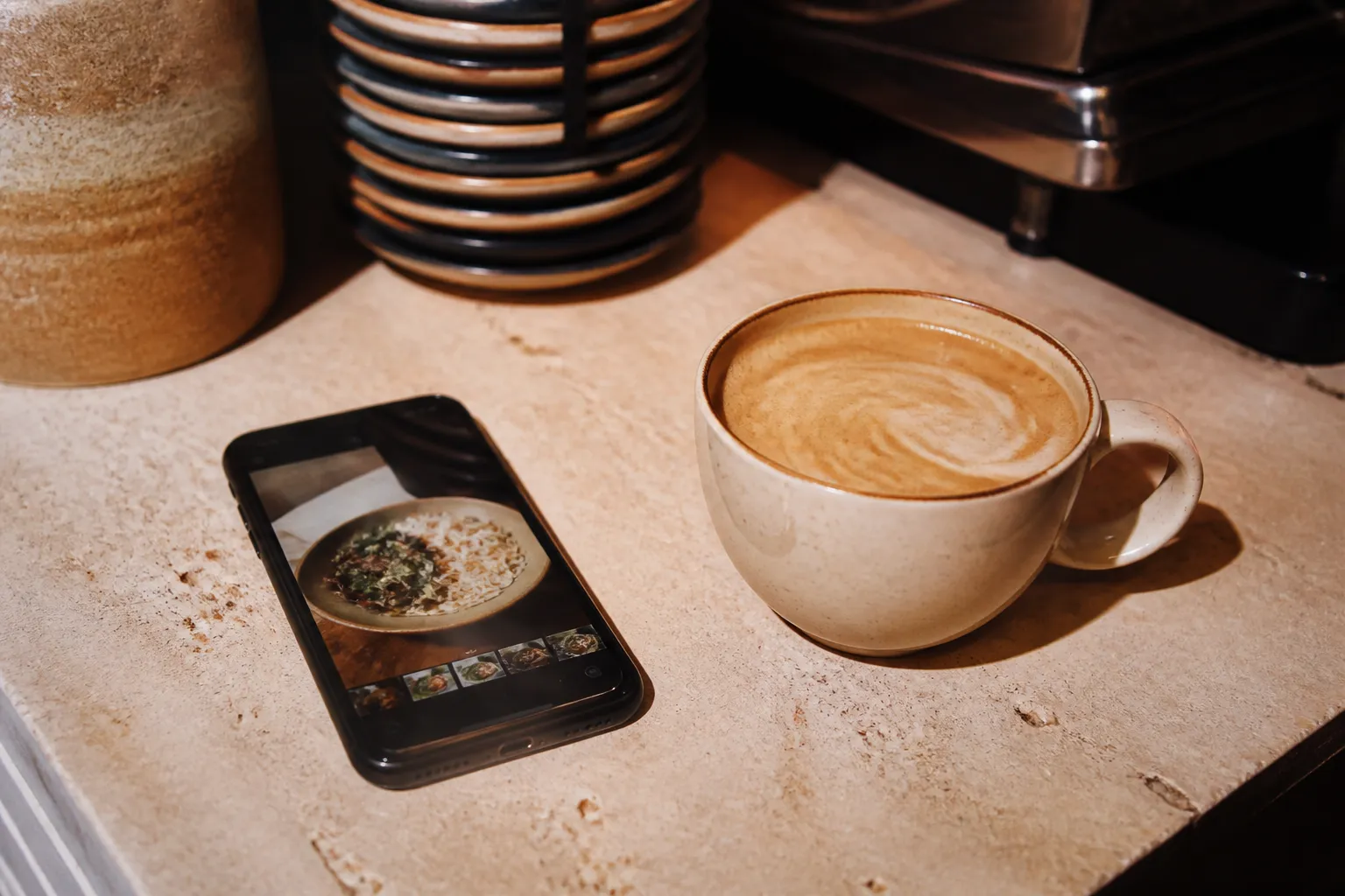 A phone showing a coffee order placed beside a fresh cup on a counter