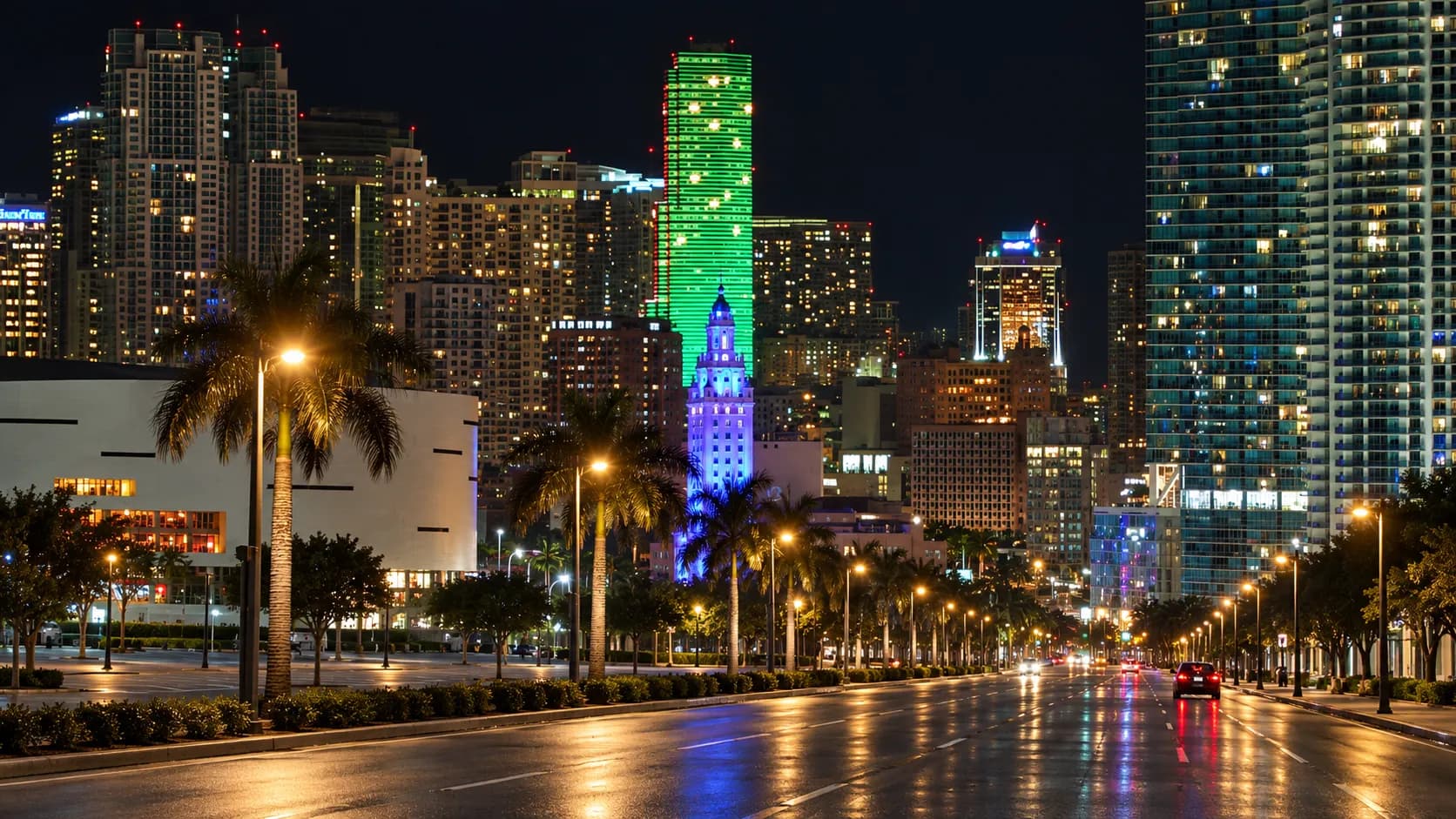 Wide multi-lane urban boulevard at night with low commercial buildings set back behind parking aprons and palms in the median
