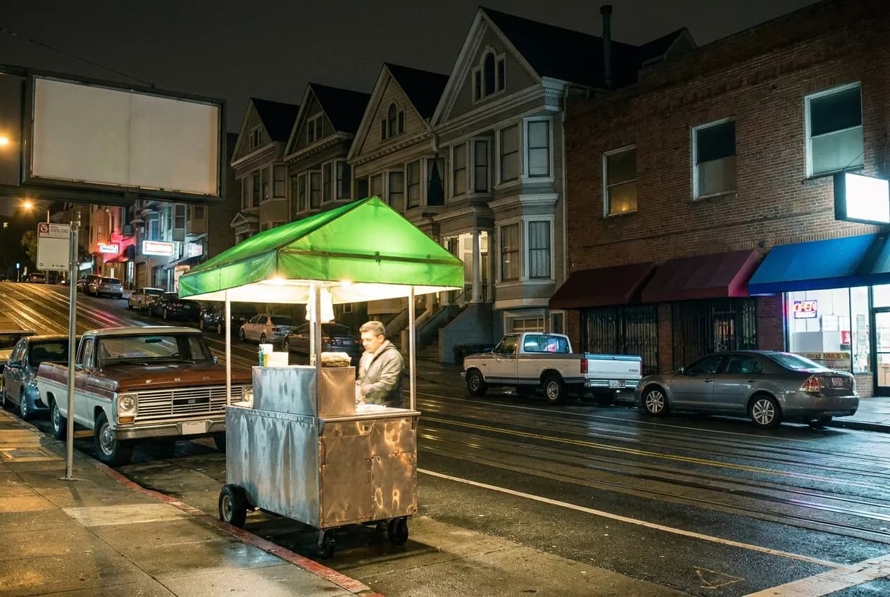 A food cart parked at a city kerb at night with a lit canopy