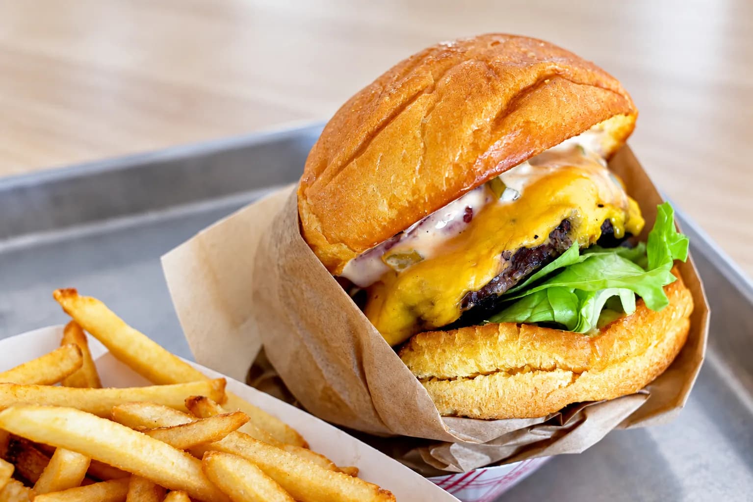 Cheeseburger in a partly unfolded paper wrapper with a soft toasted bun, a hand-formed patty with browned edges and melted cheese