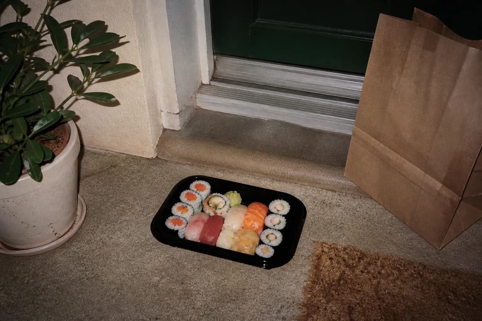 A neatly packed sushi takeout tray resting on a doorstep ready for pickup