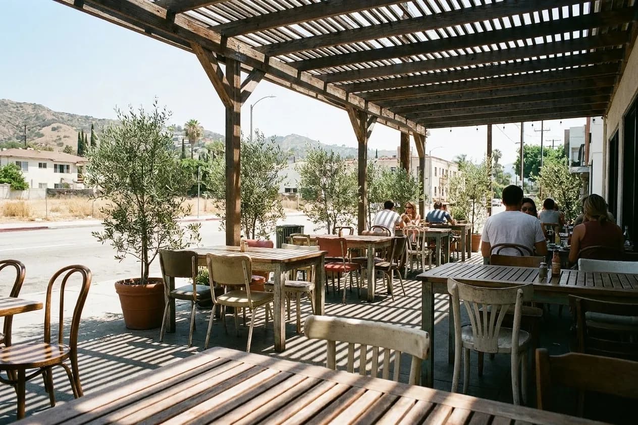 A restaurant patio at mid-morning with slatted pergola shadows falling across the tables