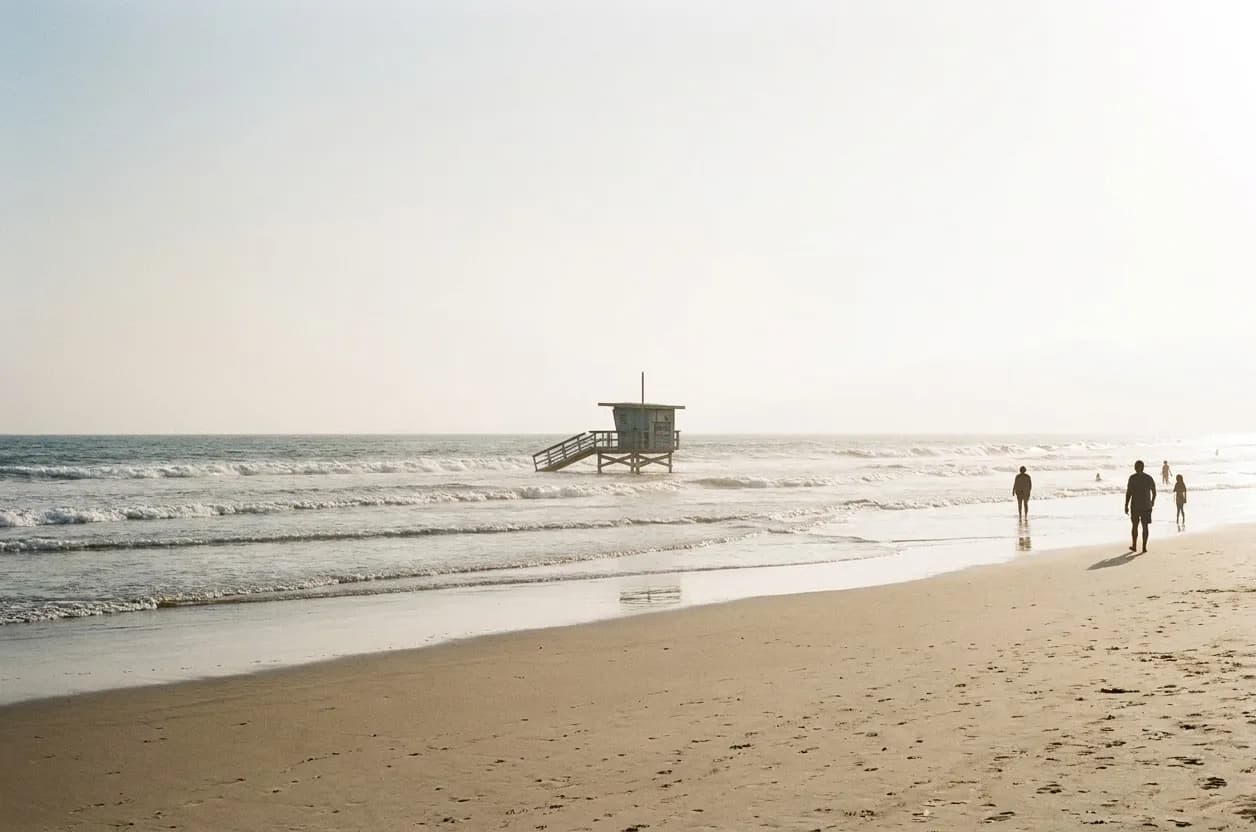 A wide sandy beach with a lifeguard tower and gentle surf under clear sky