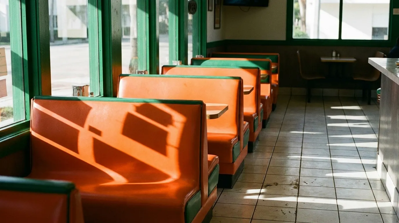 Morning sun cuts through the interior dining room windows, illuminating orange plastic booth seating and white tile floors before the lunch rush begins.