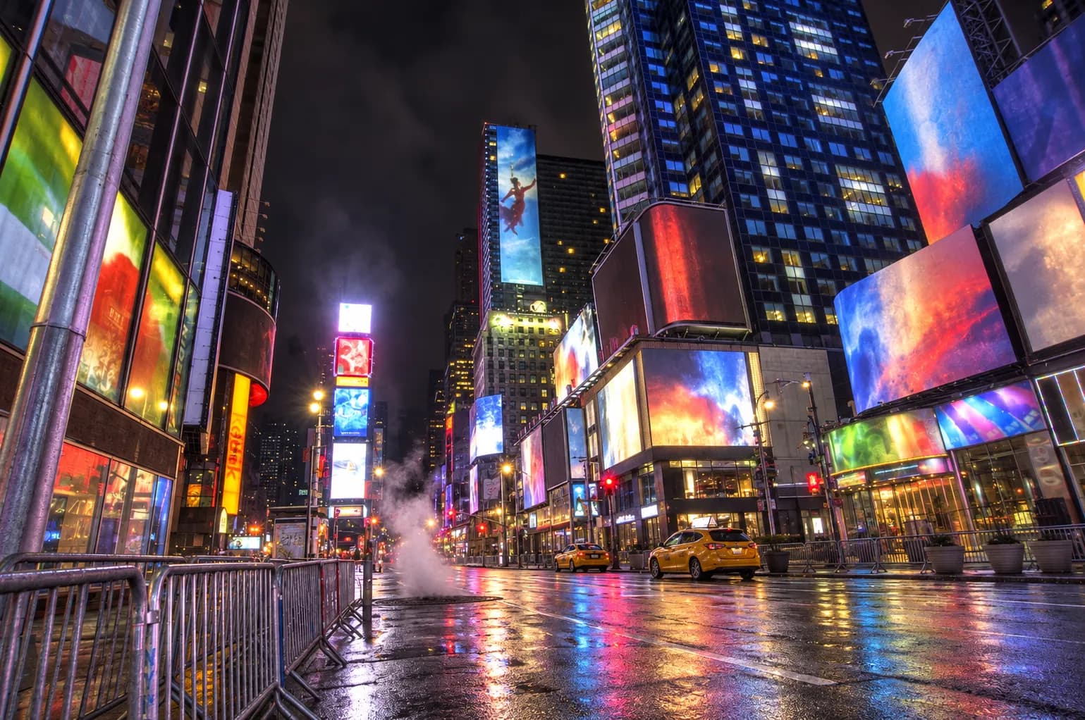 Times Square at three in the morning with illuminated advertising facades on all sides, wet asphalt reflecting colour and a near-empty pedestrian plaza