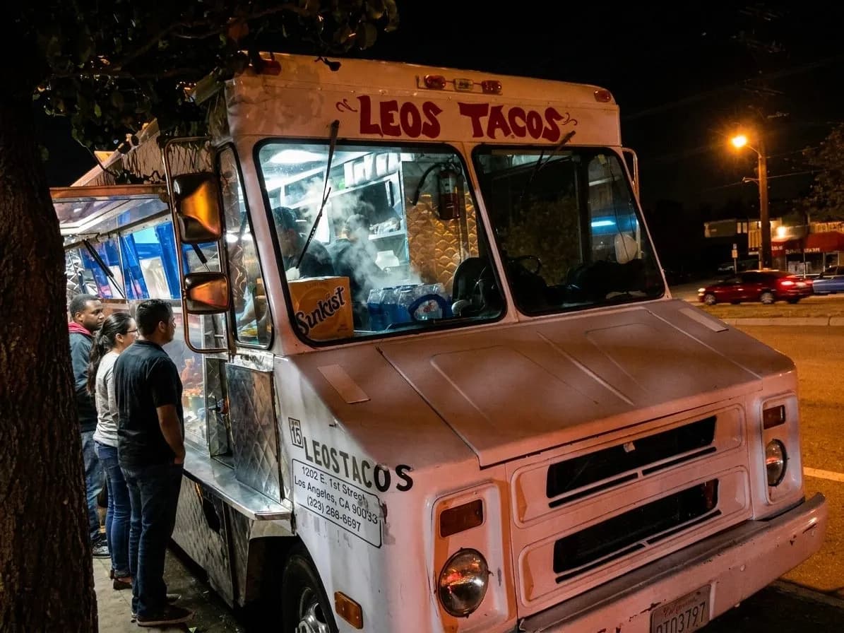 A bright Los Angeles taco truck at night with a short line and glowing grill