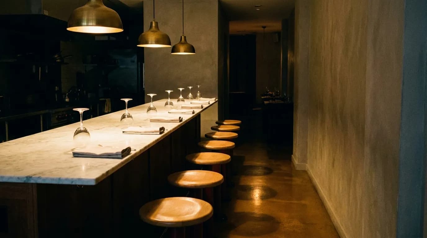 A chef's counter seen end-on with six stools, a marble top and pendant lights above
